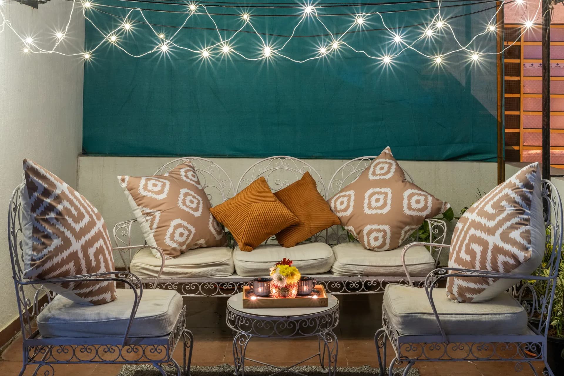 Evening terrace with a wrought-iron sofa and chairs, string lights overhead, and a lit coffee table with candles.