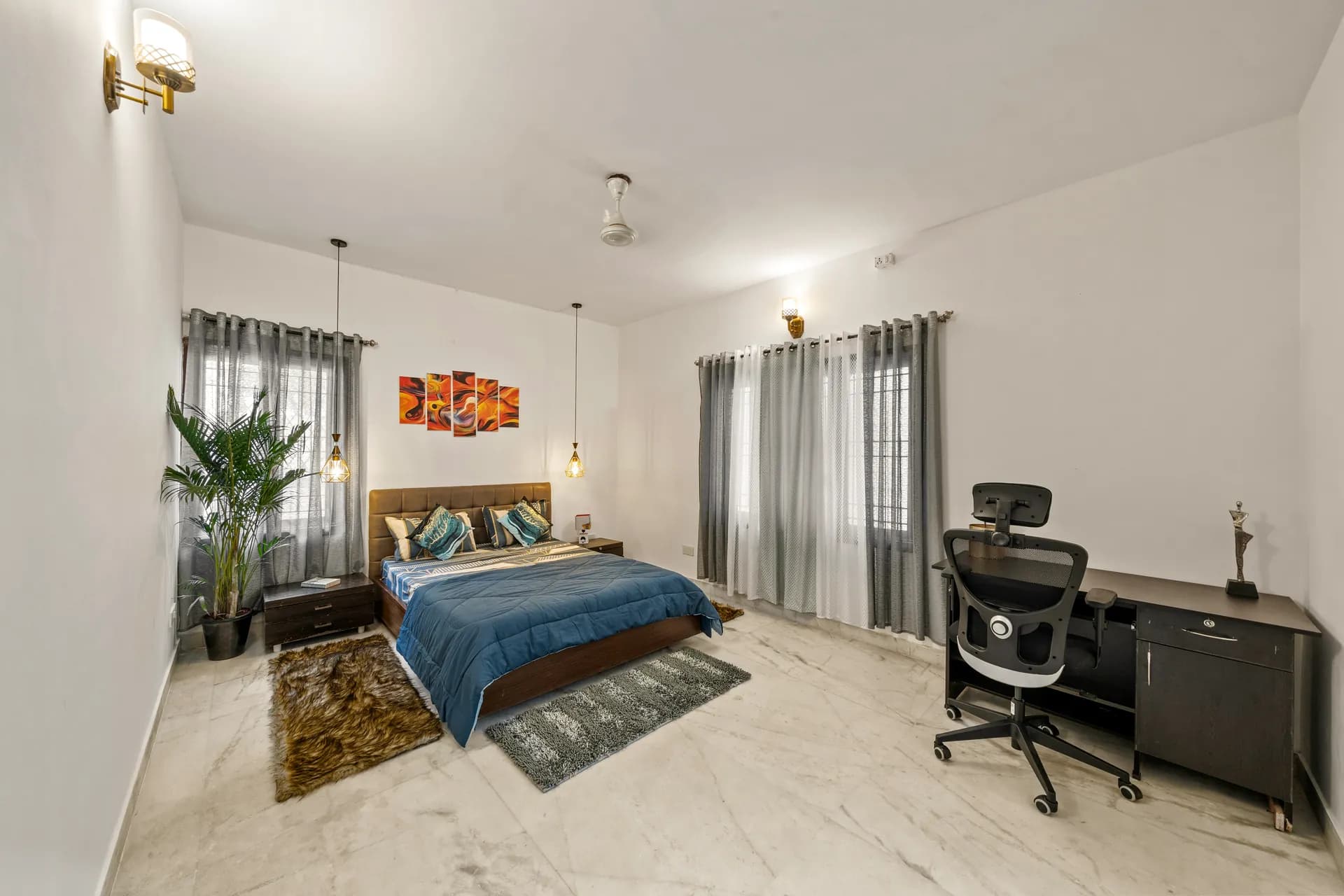 Bright bedroom with a double bed, a black office desk and chair by the window, and a potted palm.