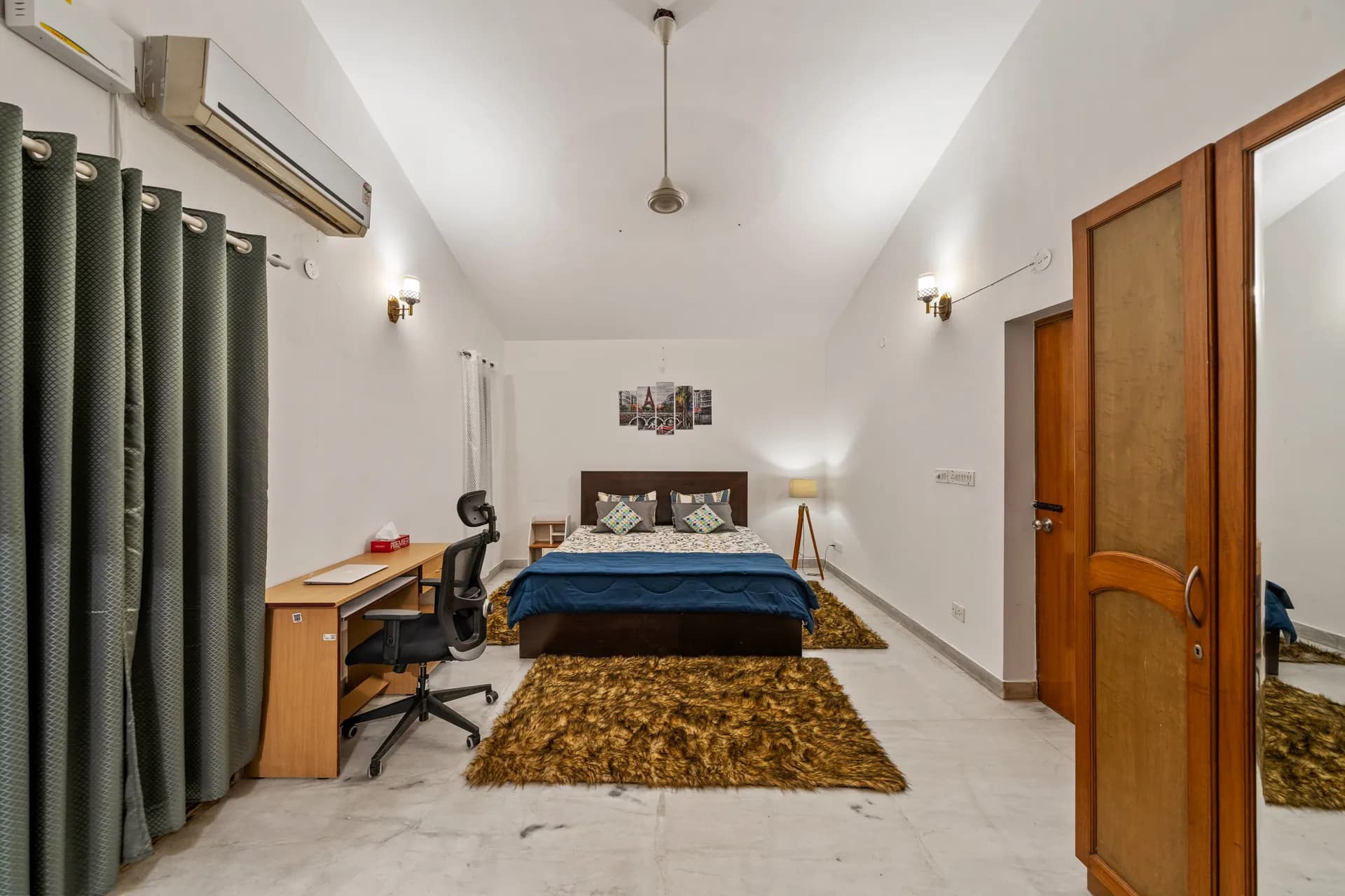 Bedroom with a double bed, wooden wardrobe, air conditioner and a small study desk with chair.