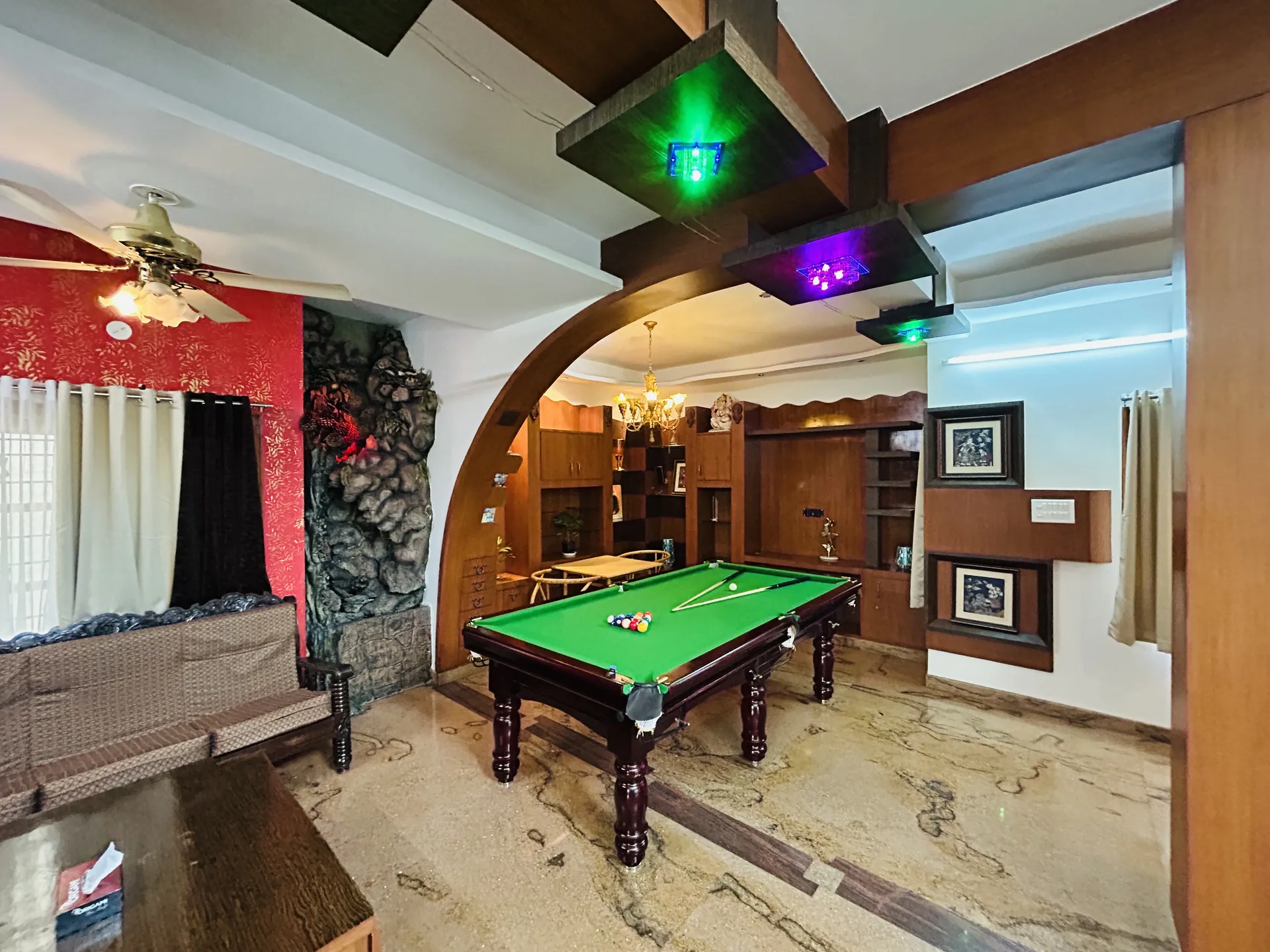Game lounge with a green-felt pool table, arched wood doorway, and a stone-effect feature wall beside the sofa.