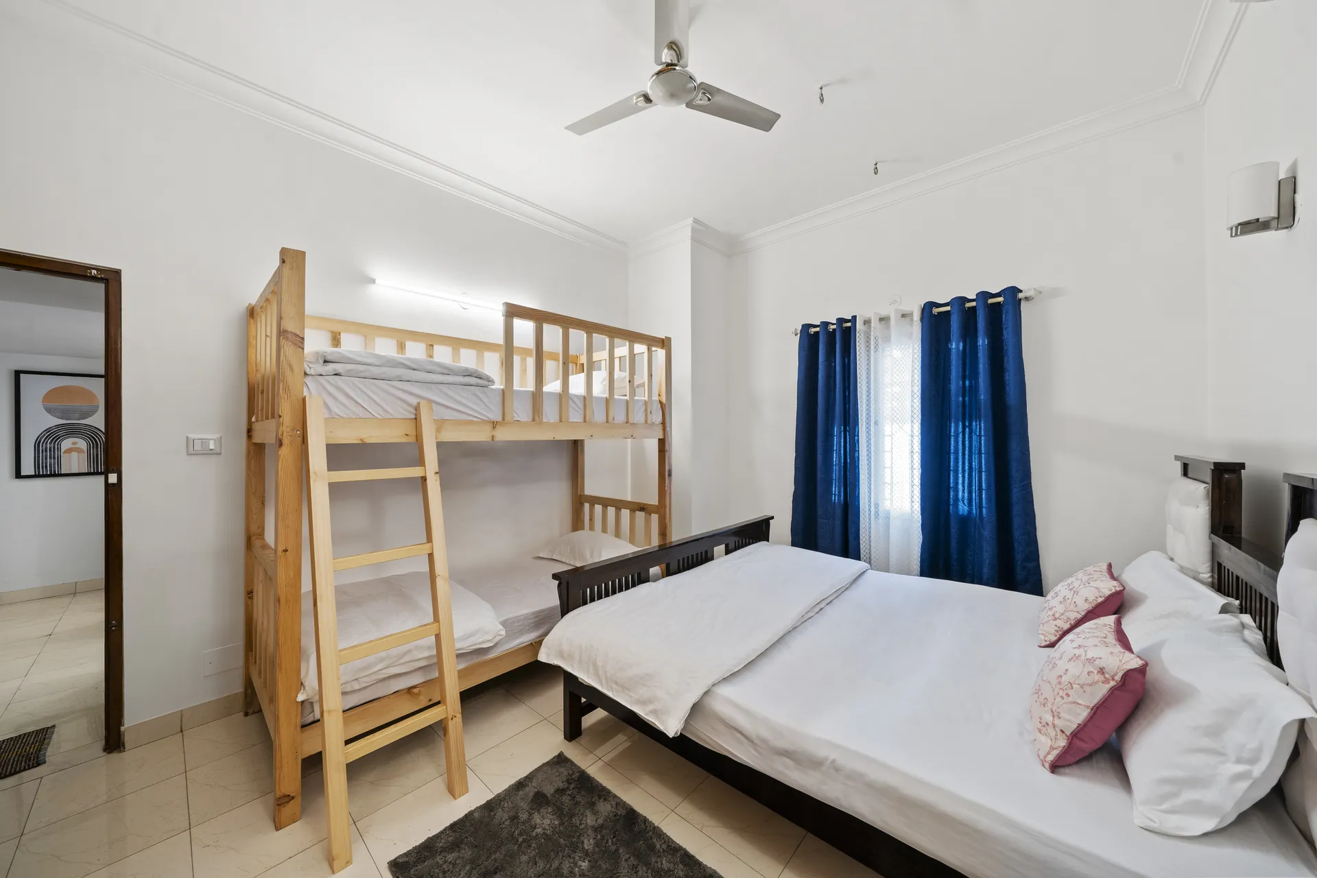 Bedroom with a wooden bunk bed beside a double bed, blue curtains and a ceiling fan.