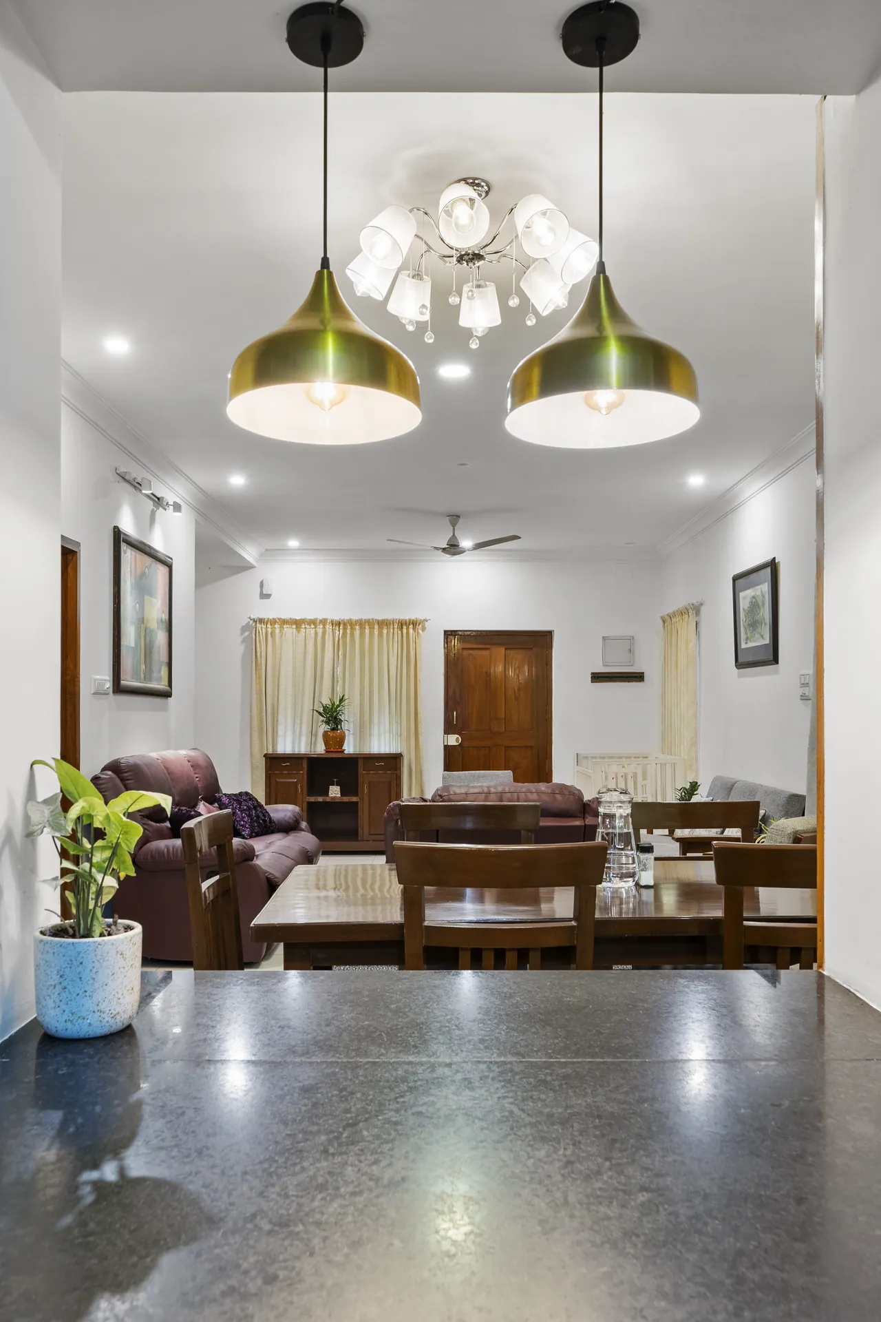 Open-plan dining table and living area with two brass pendant lights, sofas and a wooden sideboard beyond.