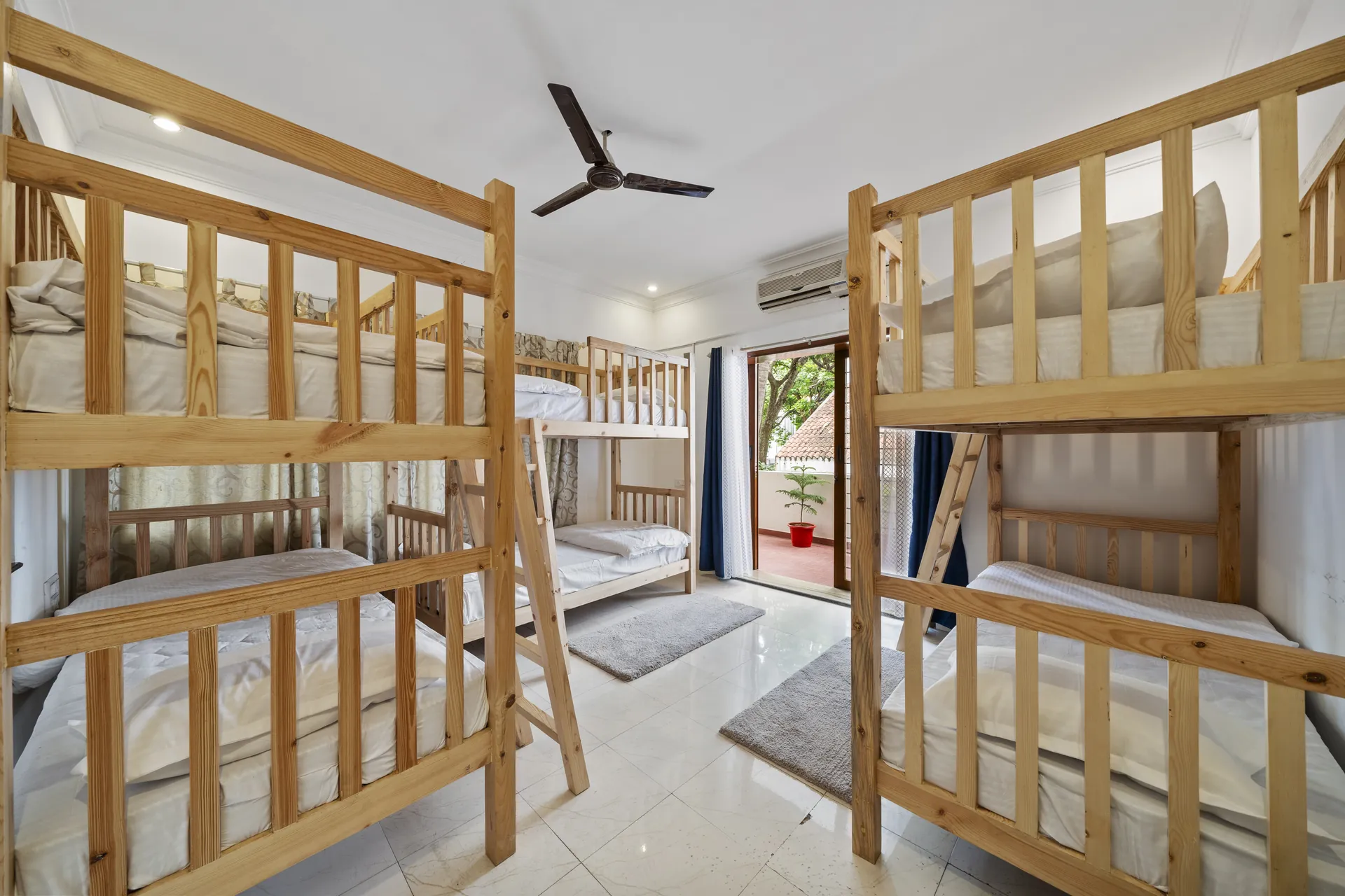 Bedroom with four bunk beds of pale wood, a ceiling fan, and a glass door opening onto a balcony.