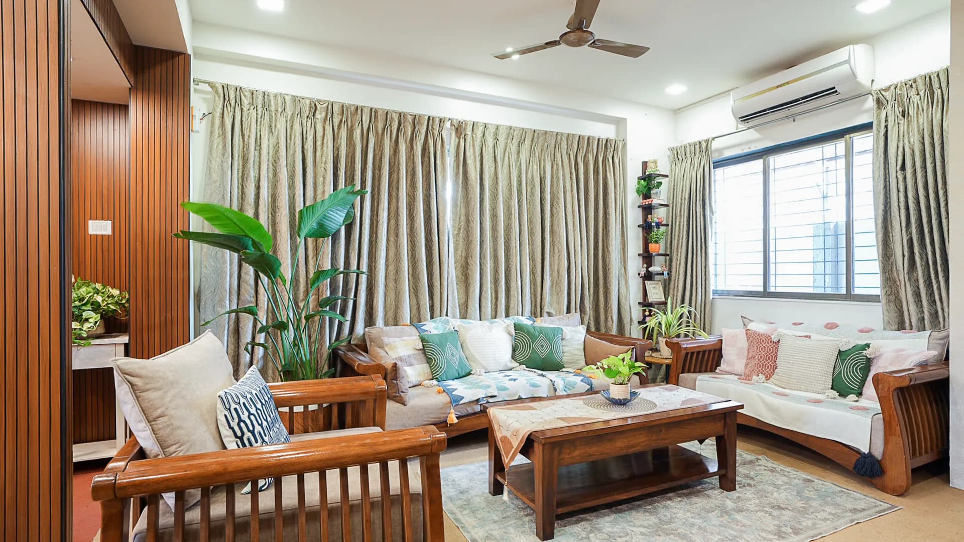 Living room with wooden sofa and armchair, green curtains, ceiling fan, and a wall-mounted air conditioner.