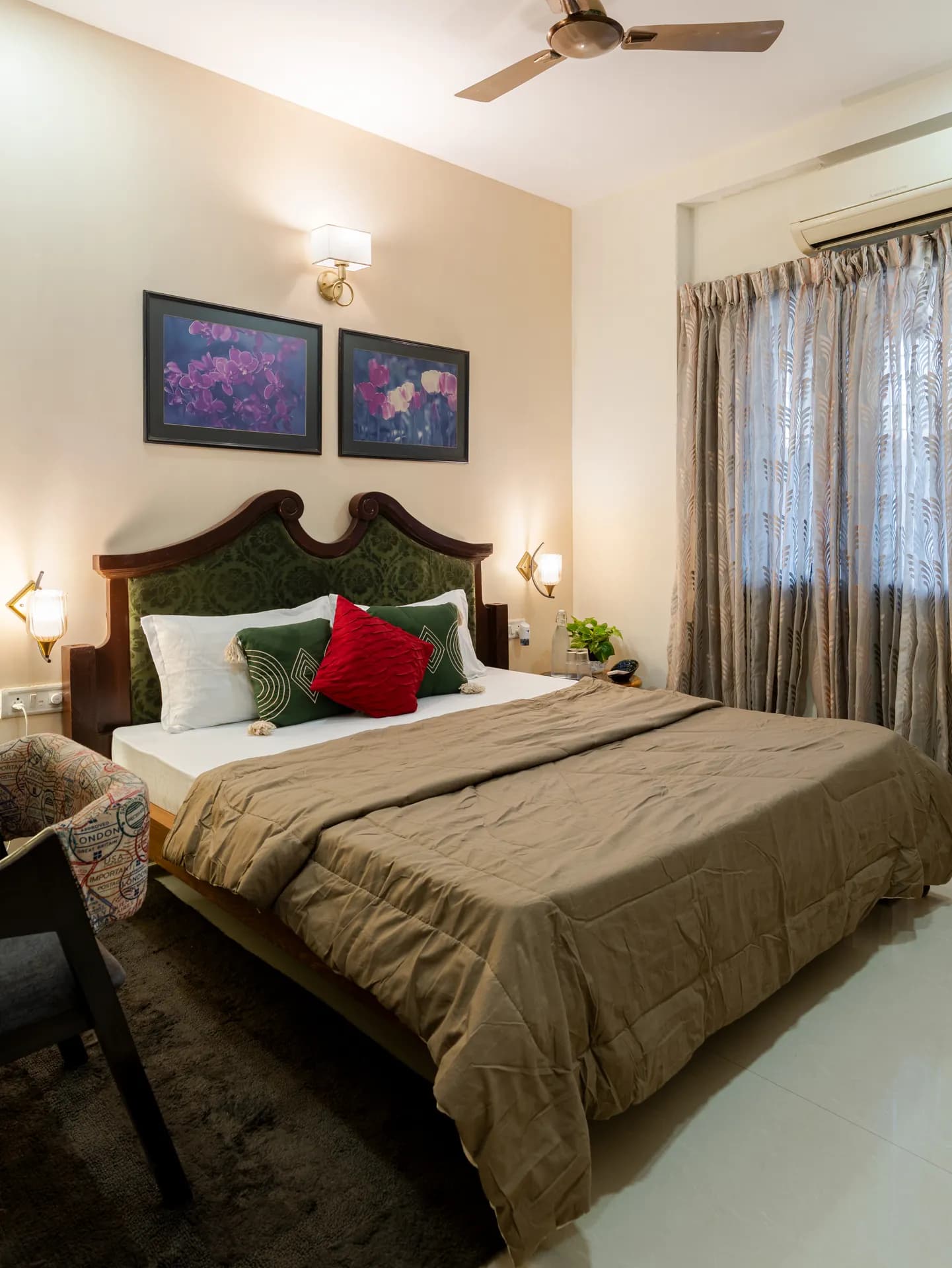Bedroom with a wooden-framed double bed, green headboard, framed floral prints, and sheer patterned curtains by the window.