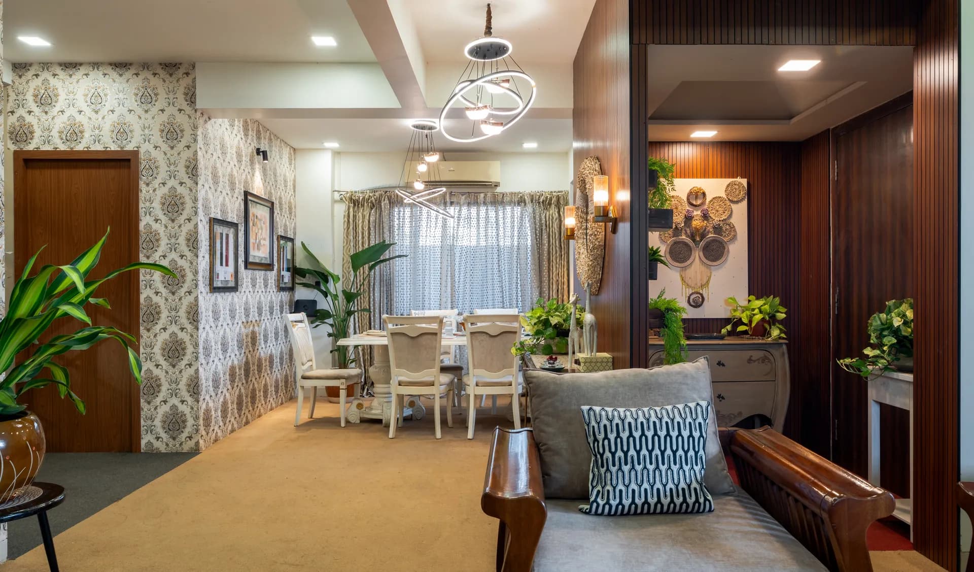 Open living and dining area with patterned feature wall, pendant ring lights, and a grey sofa with wooden arms in the foreground.