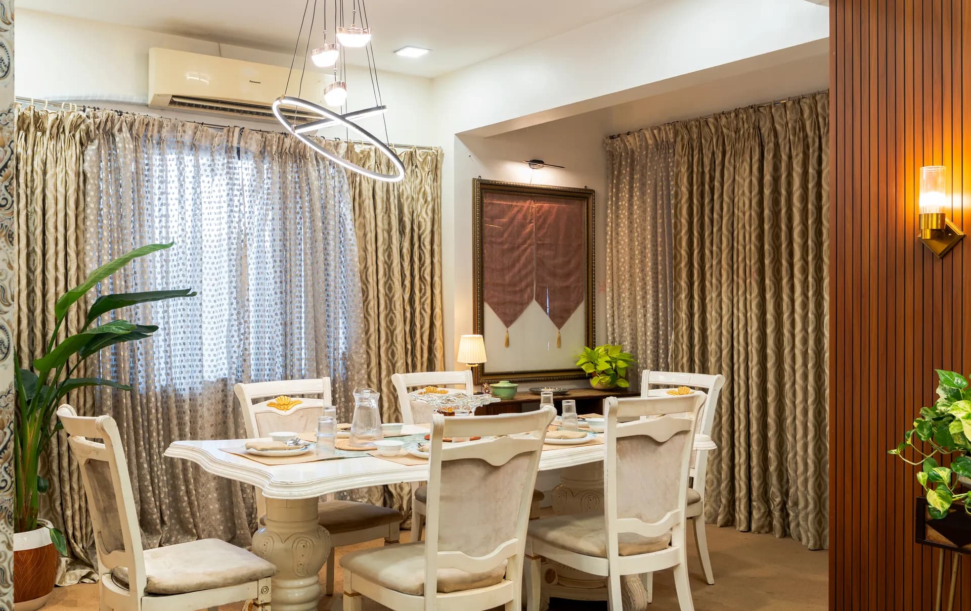 Dining room with a white table set for a meal, cream chairs, floor-length patterned curtains and a ring pendant light.