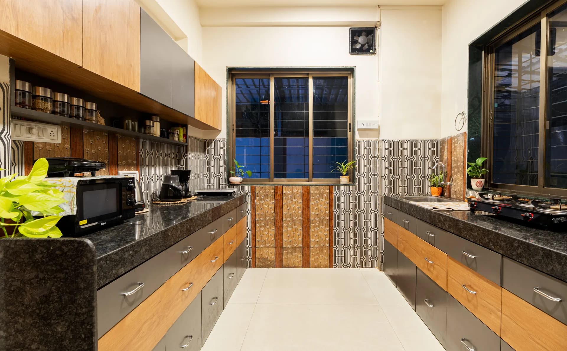 Galley kitchen with dark granite counters, wood-and-grey cabinets, a microwave and a window over the sink.
