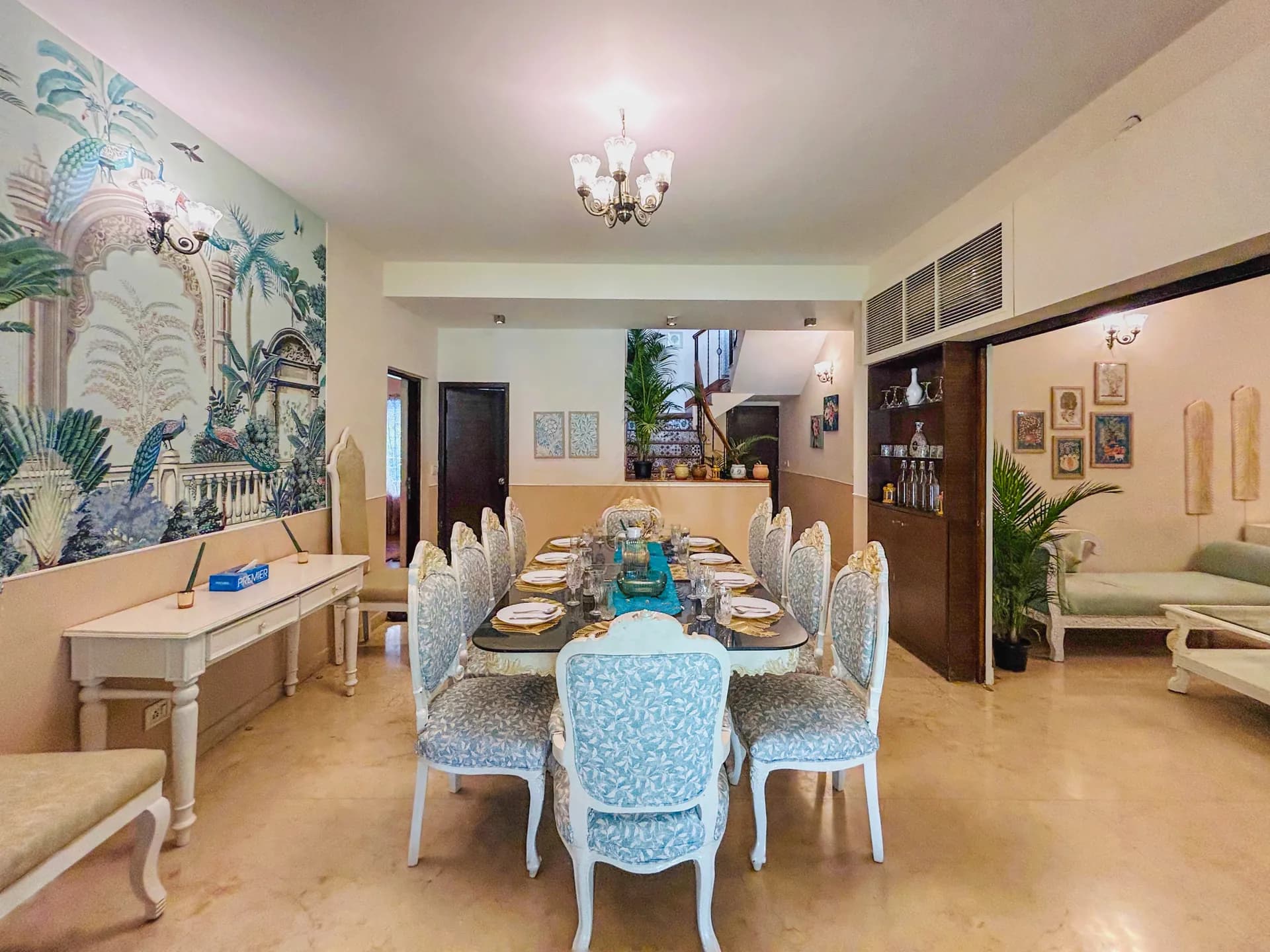 Formal dining room with a long table set for guests, mural wall, and a chandelier overhead.