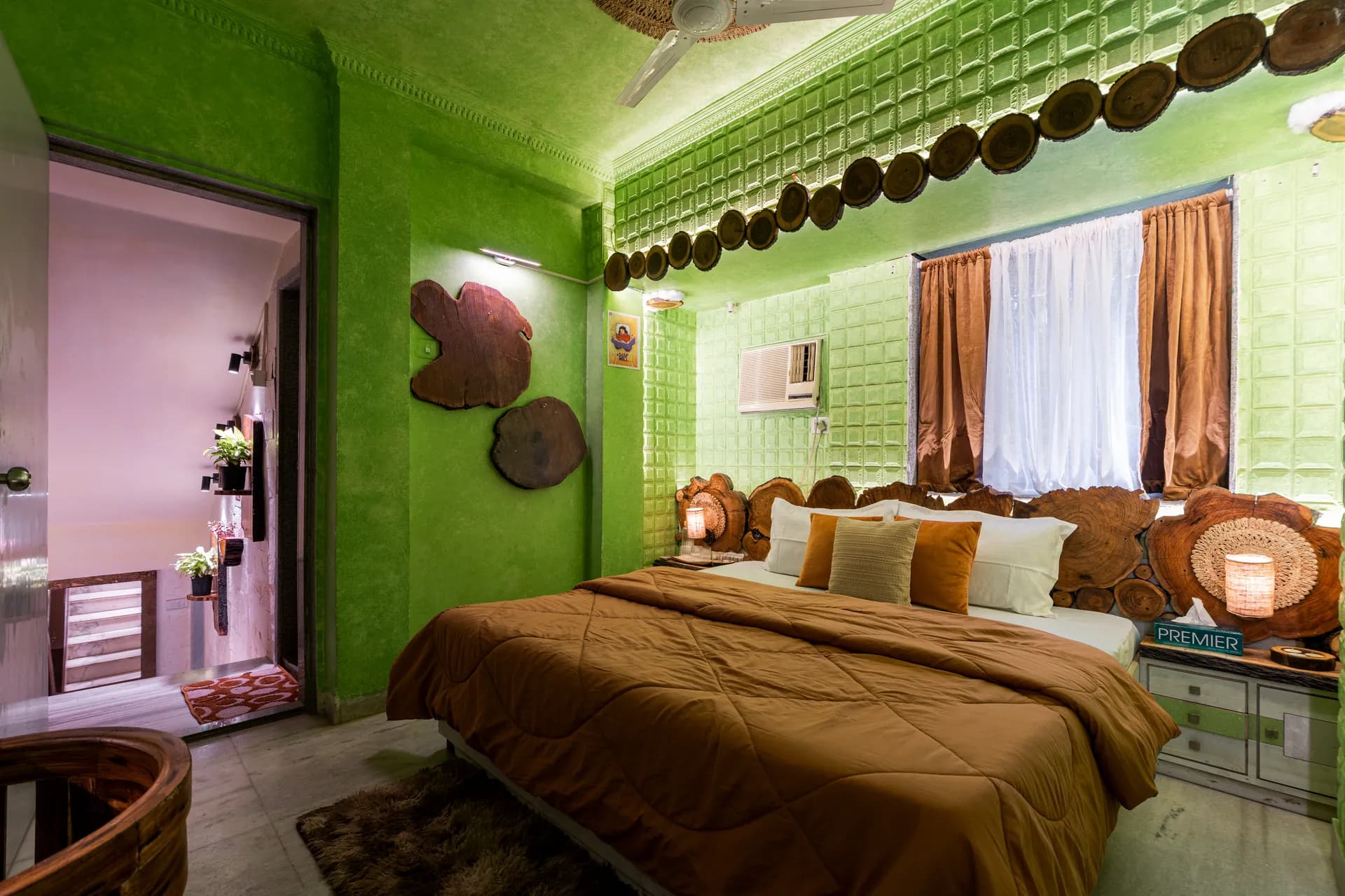 Bedroom with a king bed under green textured walls, wood slice headboard, and a window with brown curtains.