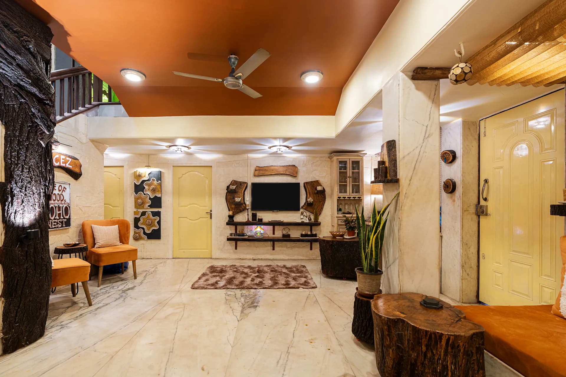 Open living area with marble floors, a wall-mounted TV, carved wood accents and orange armchairs.