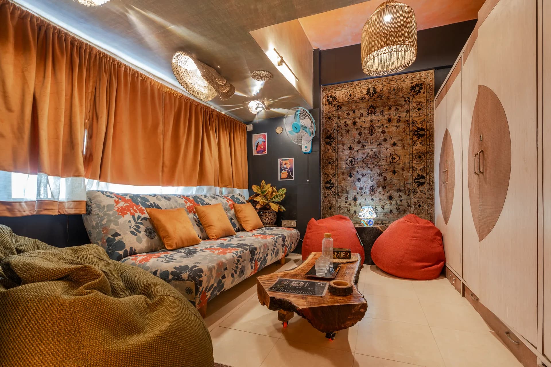 Lounge with floral sofa, orange velvet curtains, woven pendant lamps, and a live-edge wooden coffee table.