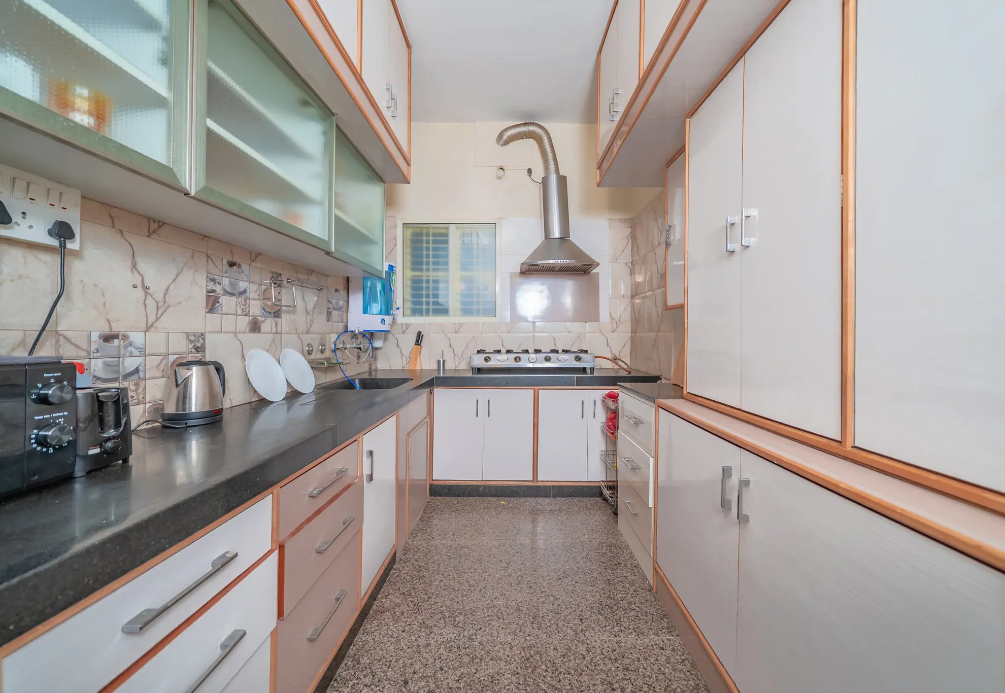 Galley kitchen with grey countertops, glass-front wall cabinets, and a stainless steel hood over the gas hob.