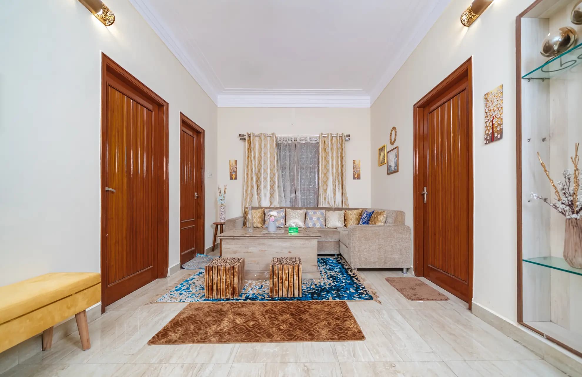 Lounge with a beige L-shaped sofa, blue patterned rug, wooden coffee table and matching stools.