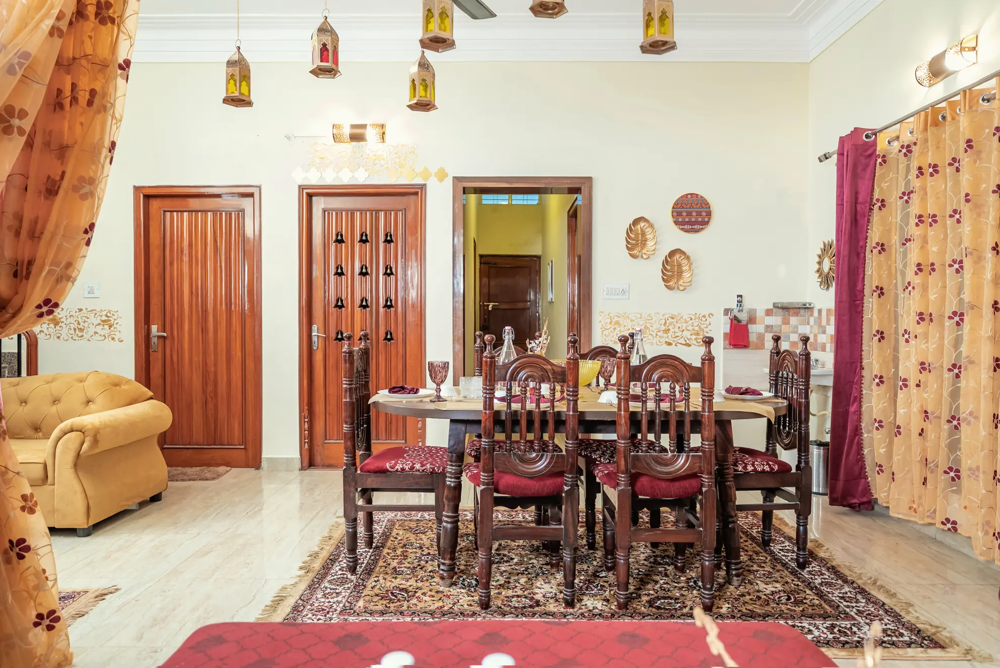 Dining room with a wooden table and six carved chairs on a patterned rug, with decorative lanterns overhead.