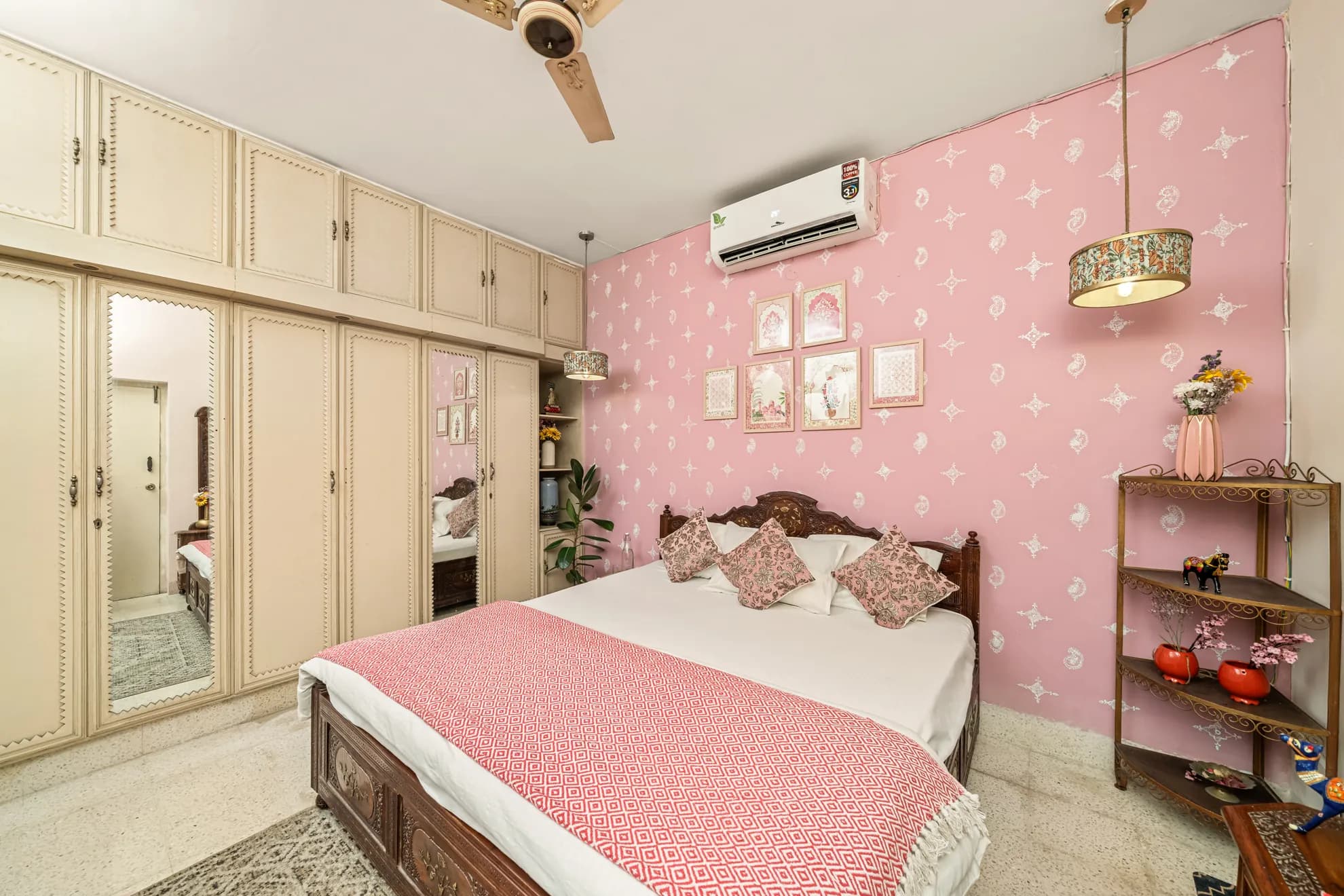 Bedroom with pink patterned wall, king bed with red throw, and built-in cream wardrobes with mirrored doors.