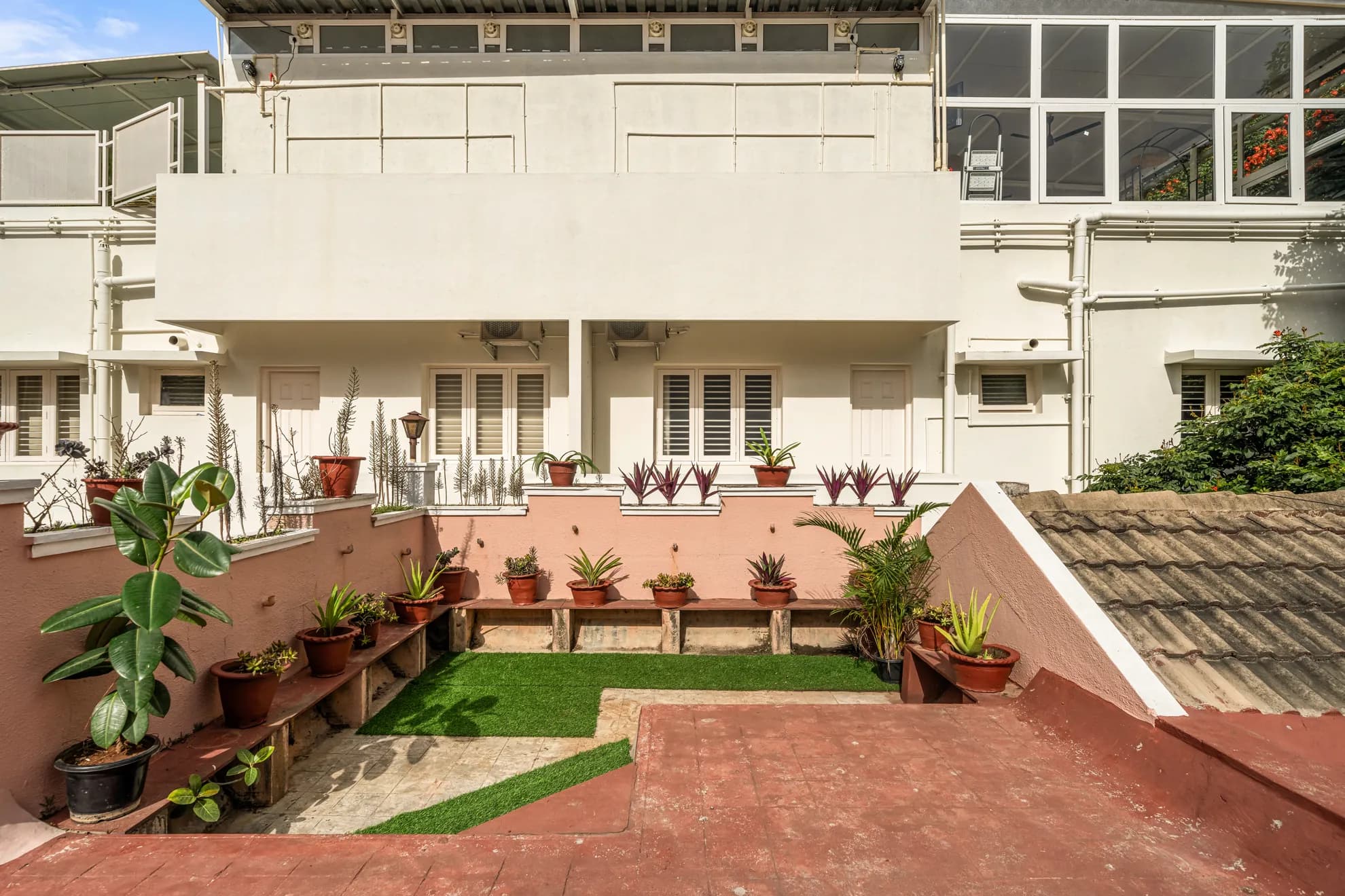Rear courtyard terrace with potted plants on tiered ledges, artificial grass patches, and a tiled floor.
