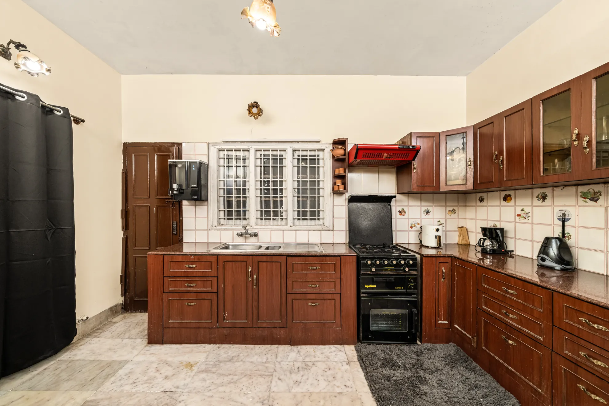 Kitchen with dark wood cabinets, black gas range and oven, and a steel sink under a barred window.