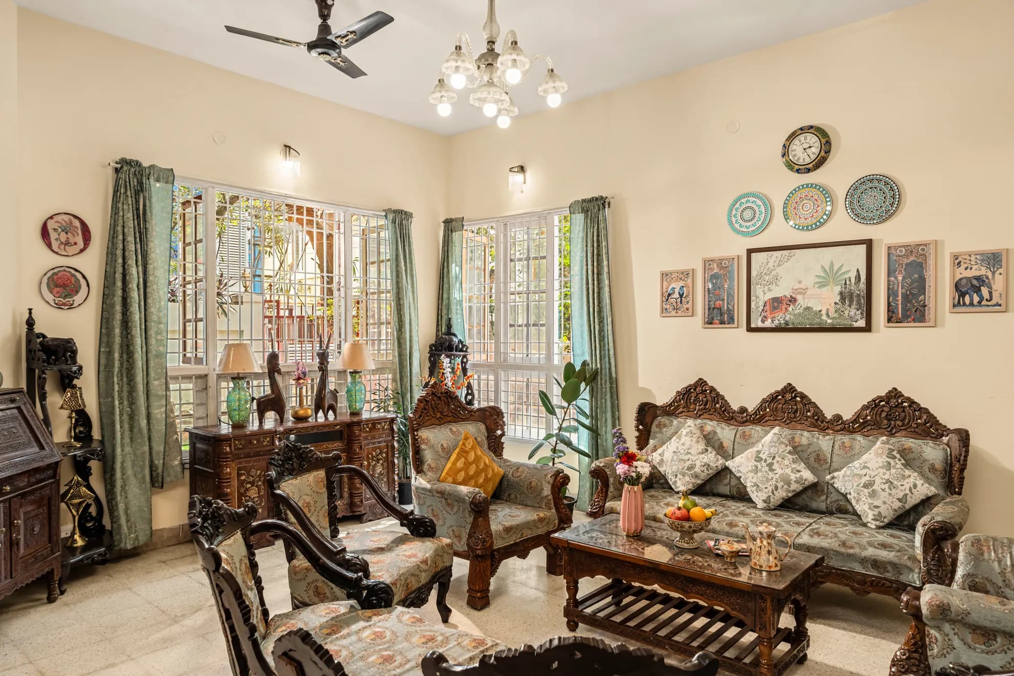 Ornate carved wooden sofa and armchairs in a living room with a ceiling fan, chandelier and wall plates.