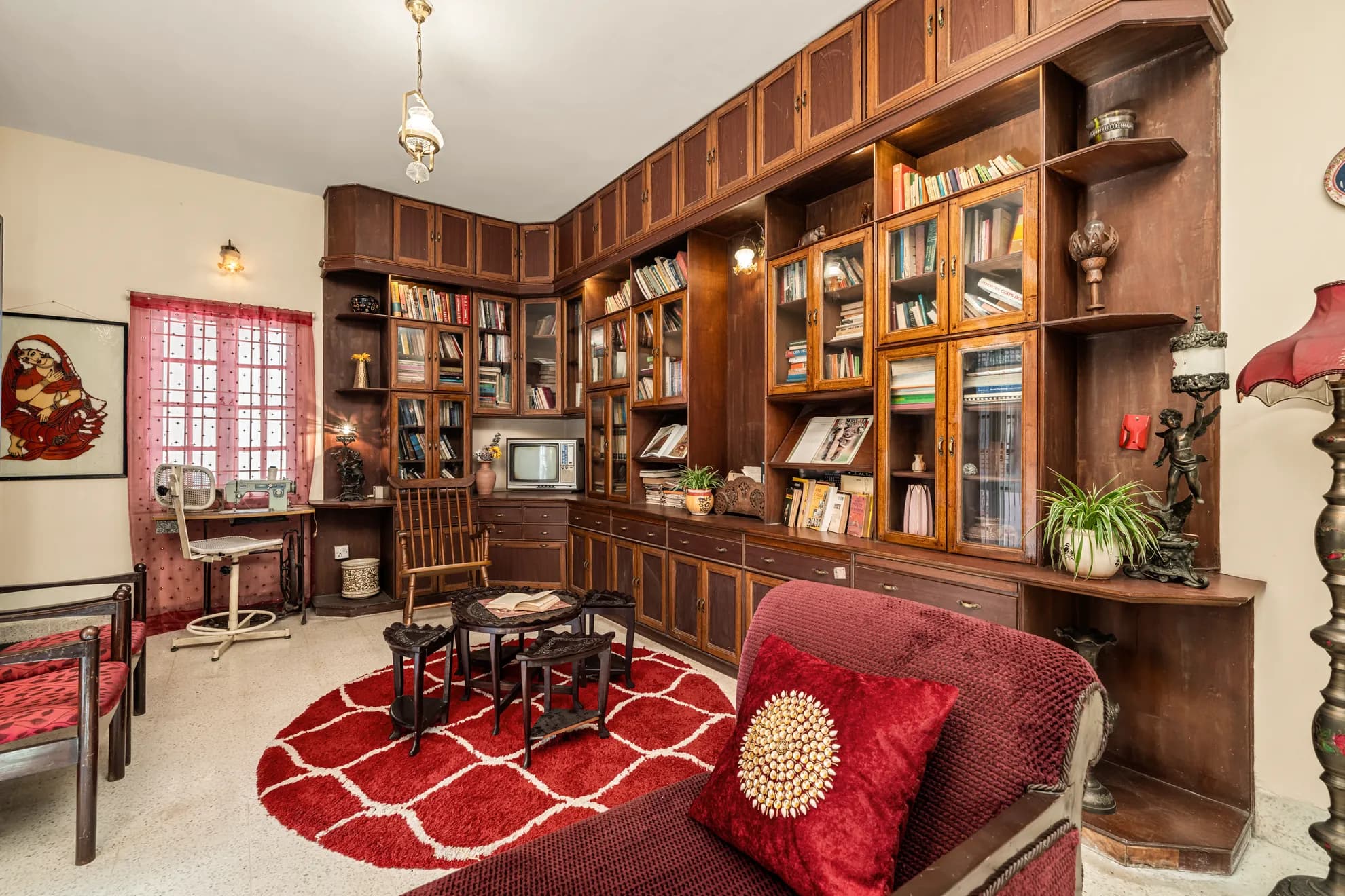 Living room with a full wall of dark wood glazed bookcases, a small CRT television, and a red shag rug.