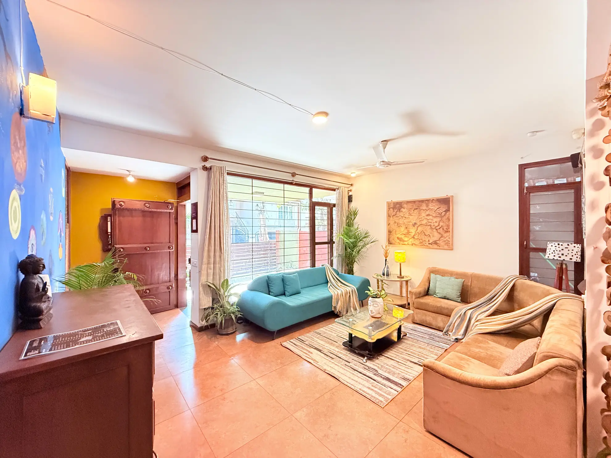 Living room with teal sofa, tan sofas, glass coffee table and a large window onto the garden.