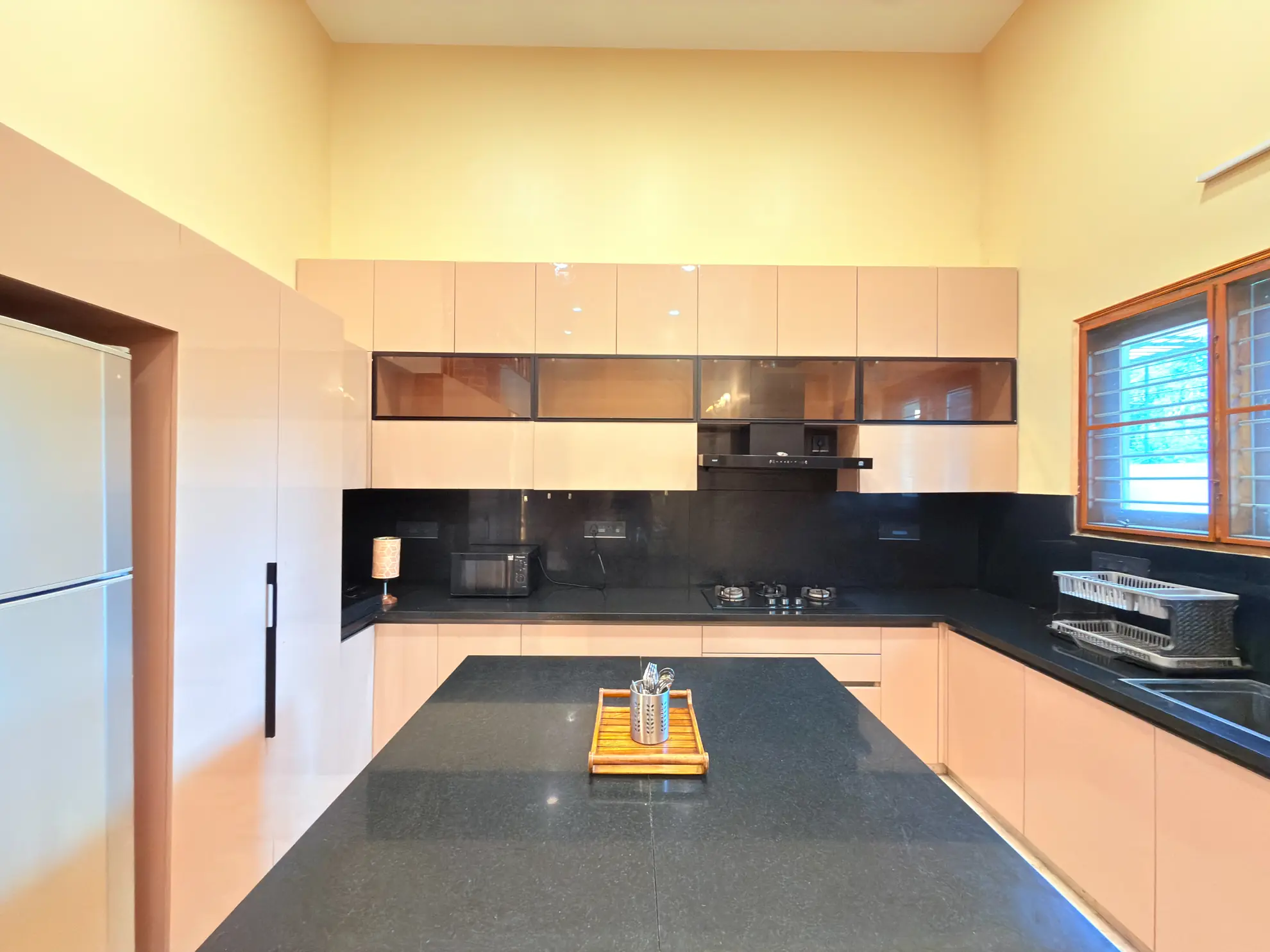 Kitchen with dark granite island, peach cabinets, glass-front wall units and a microwave on the black splashback.