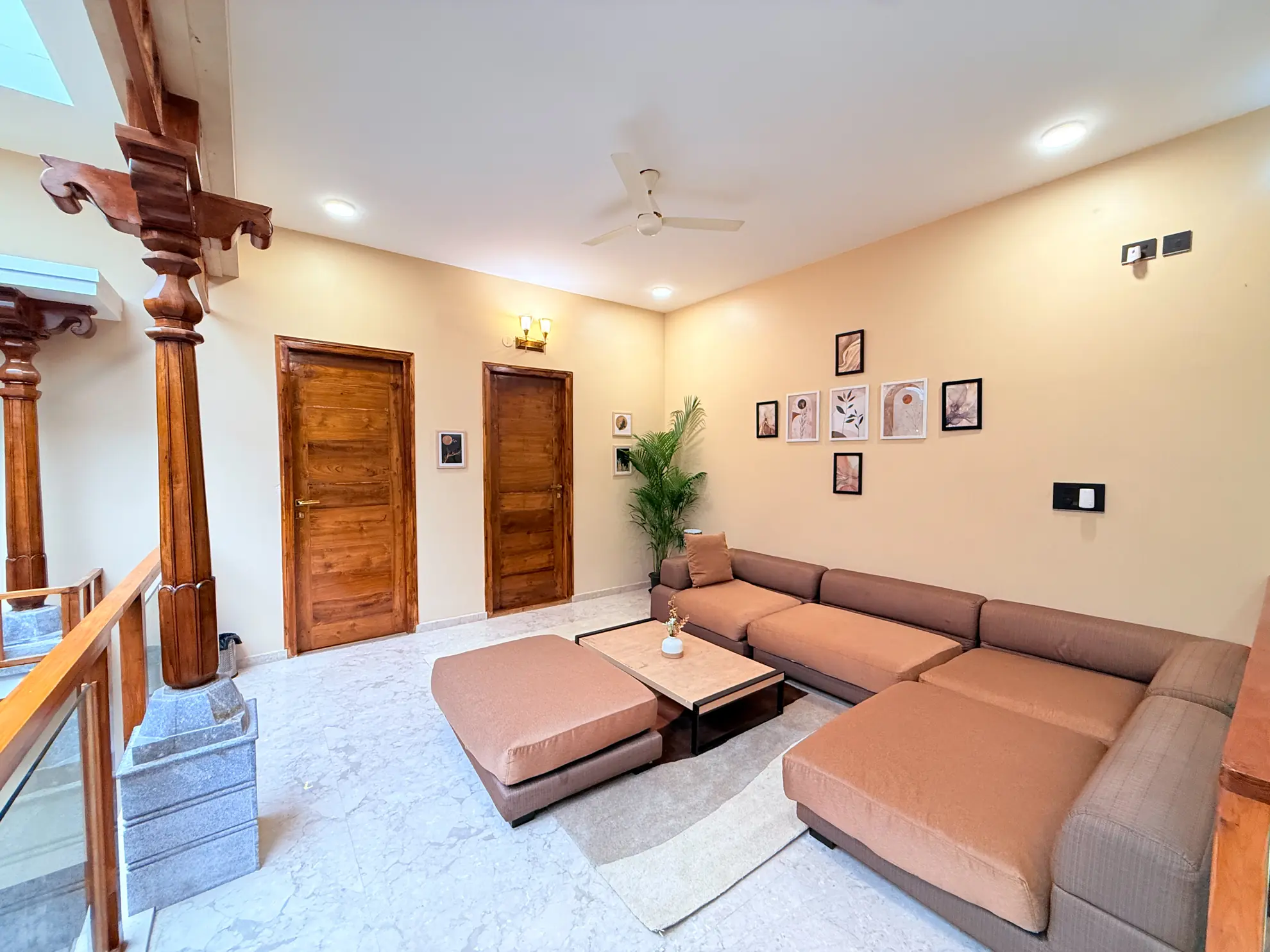 Living room with a large brown sectional sofa, wooden doors, and framed botanical prints on the wall.