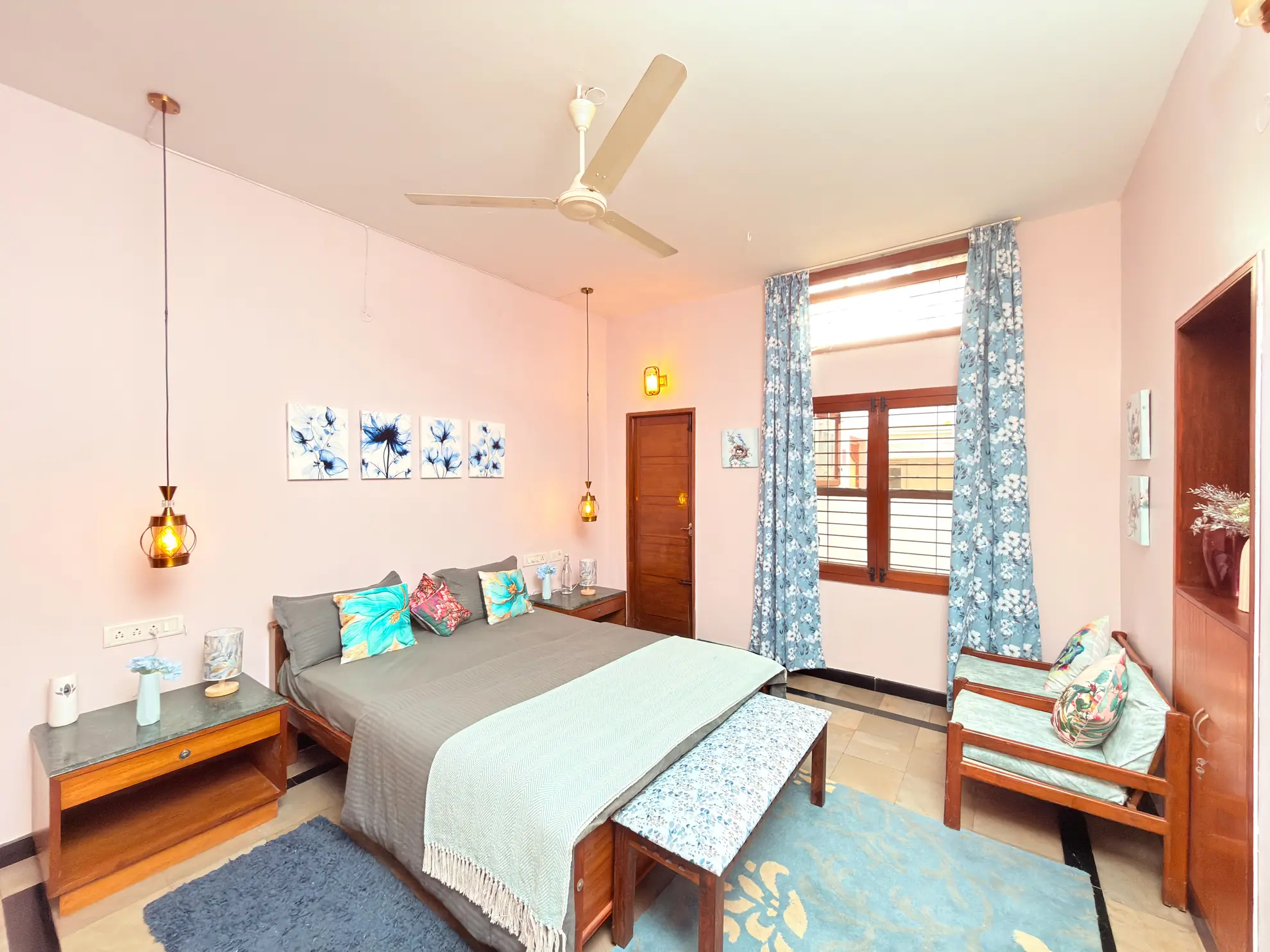 Bedroom with a double bed, pink walls, blue floral curtains and an armchair by the window.