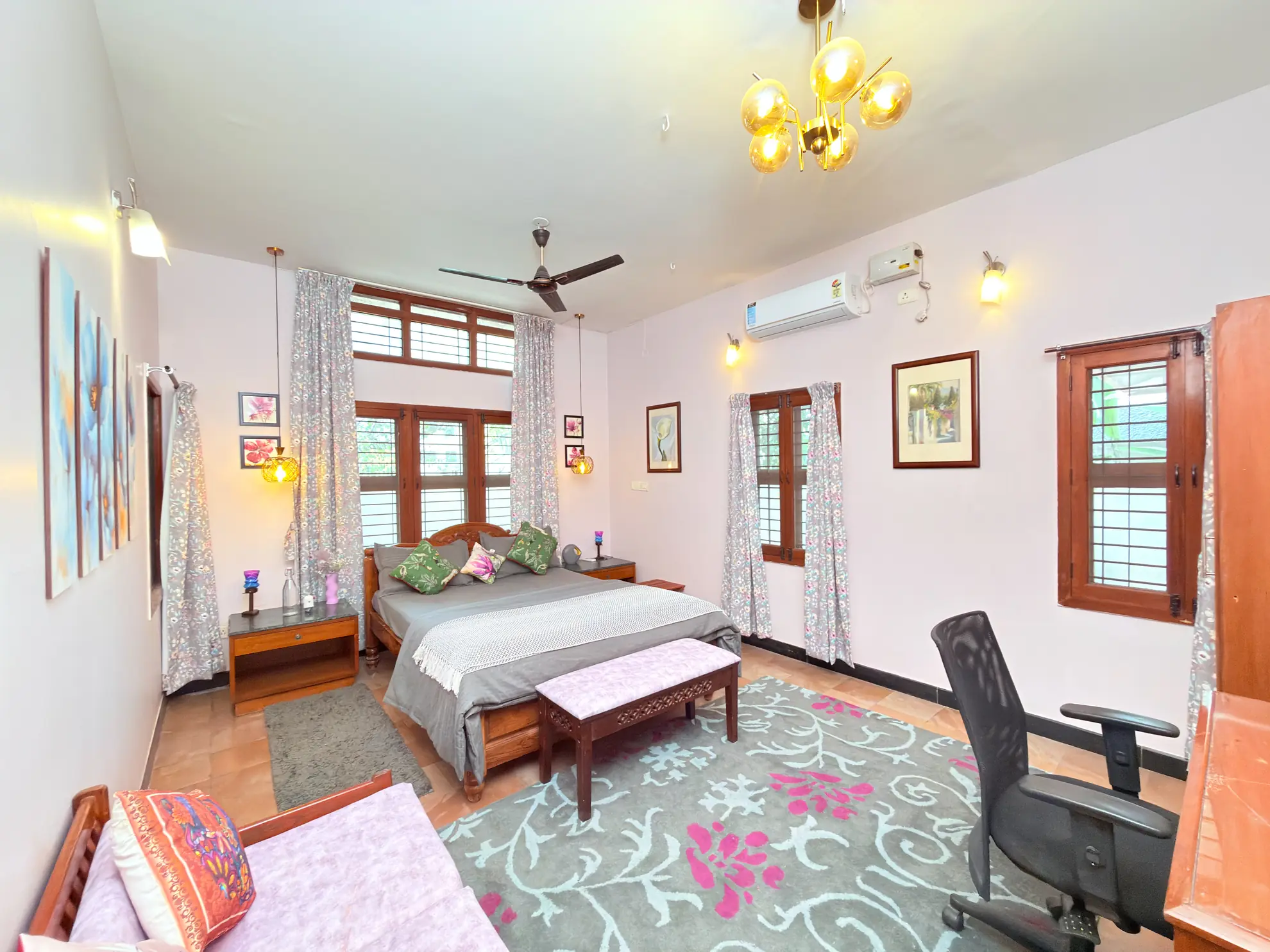 Bedroom with a double bed, wall-mounted air conditioning, a desk chair and a patterned rug under a glass chandelier.