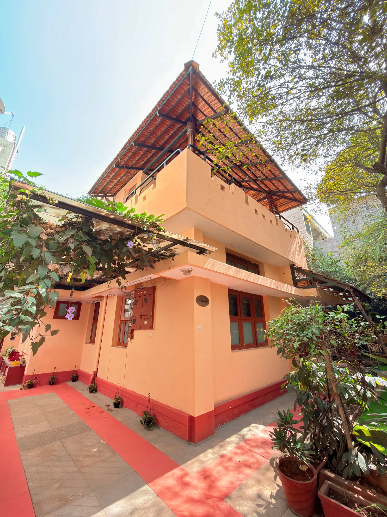 Two-storey peach villa with a tiled red-edged forecourt, potted plants and a covered balcony above.