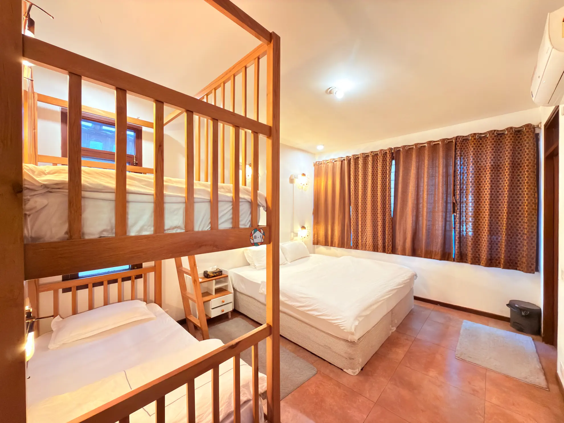 Bedroom with bunk beds and a double bed, curtained window, wall-mounted air conditioner visible.