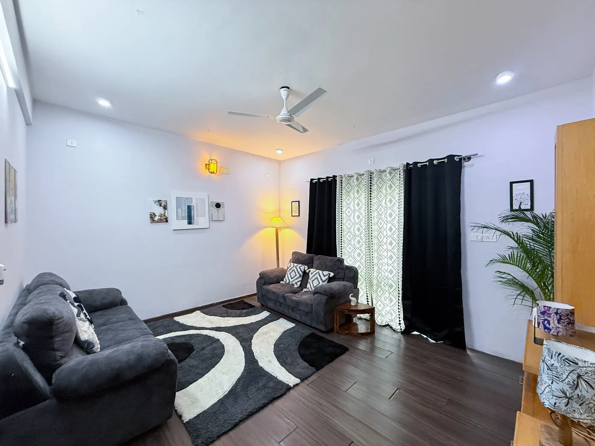 Living room with grey sofas, a patterned rug, floor lamp and black curtains by the window.