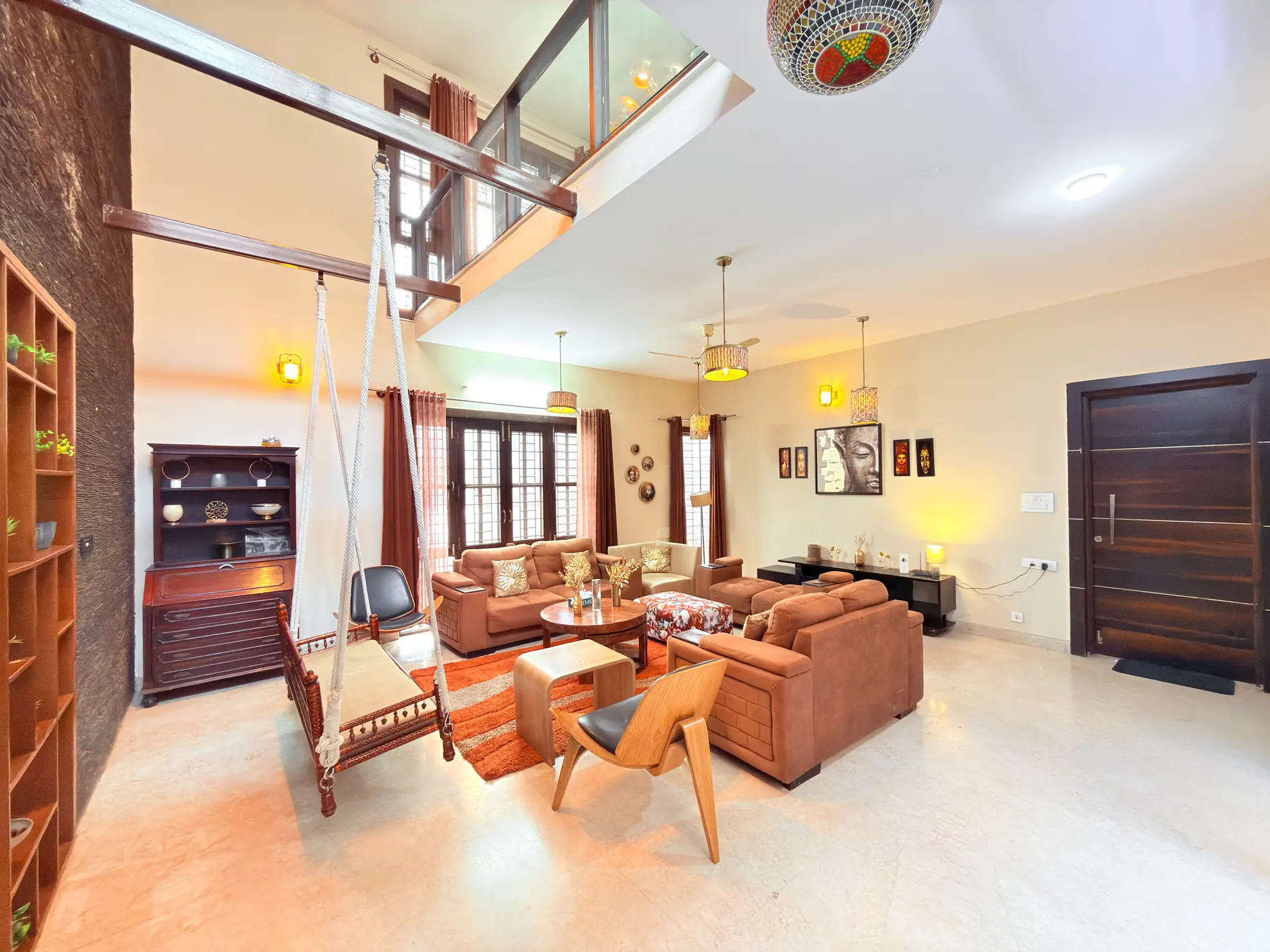 Double-height living room with brown leather sofas, a hanging wooden swing, and a loft balcony overhead.