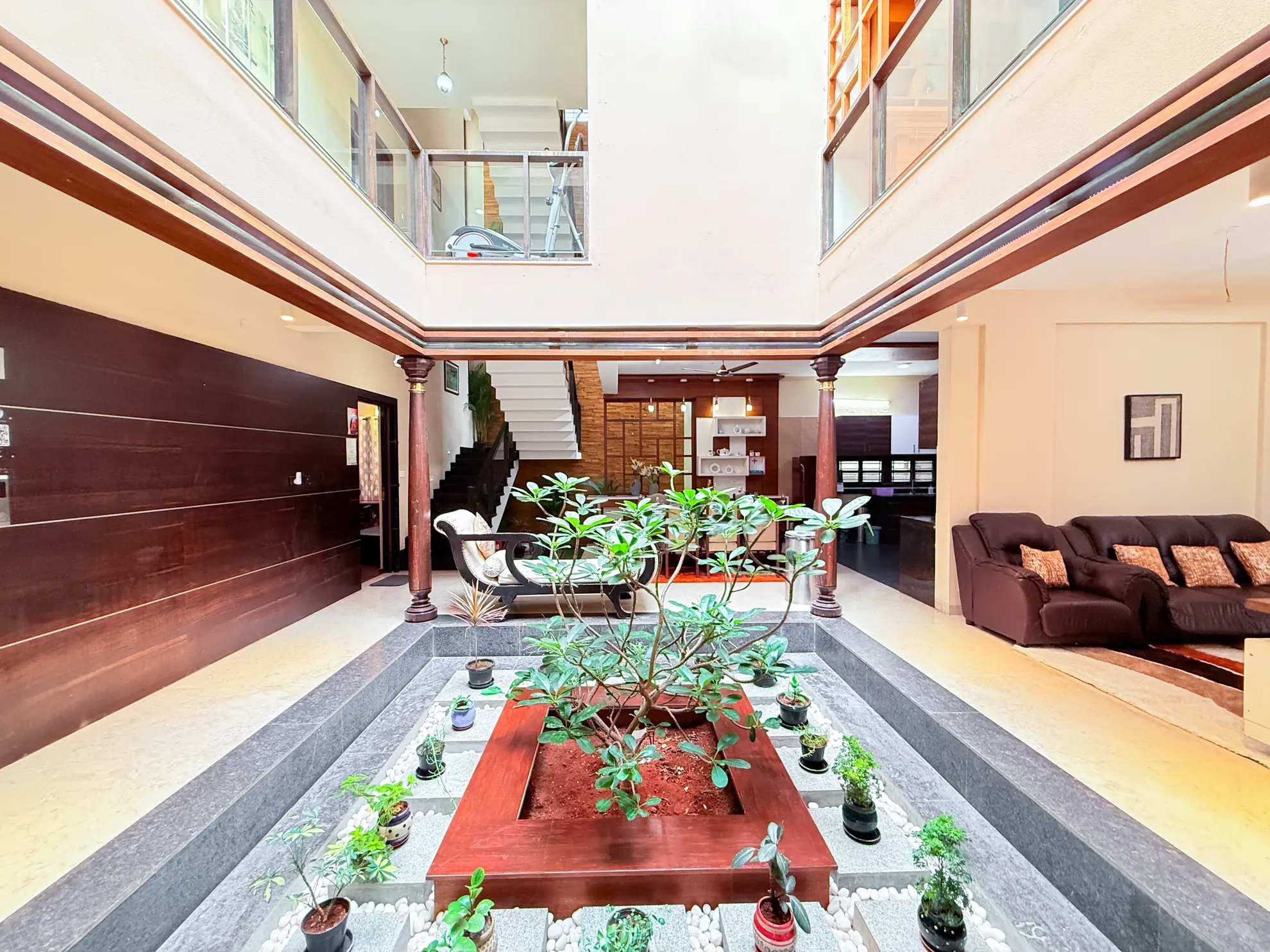 Two-storey indoor courtyard with a raised planter, potted plants and a brown sofa beside it.