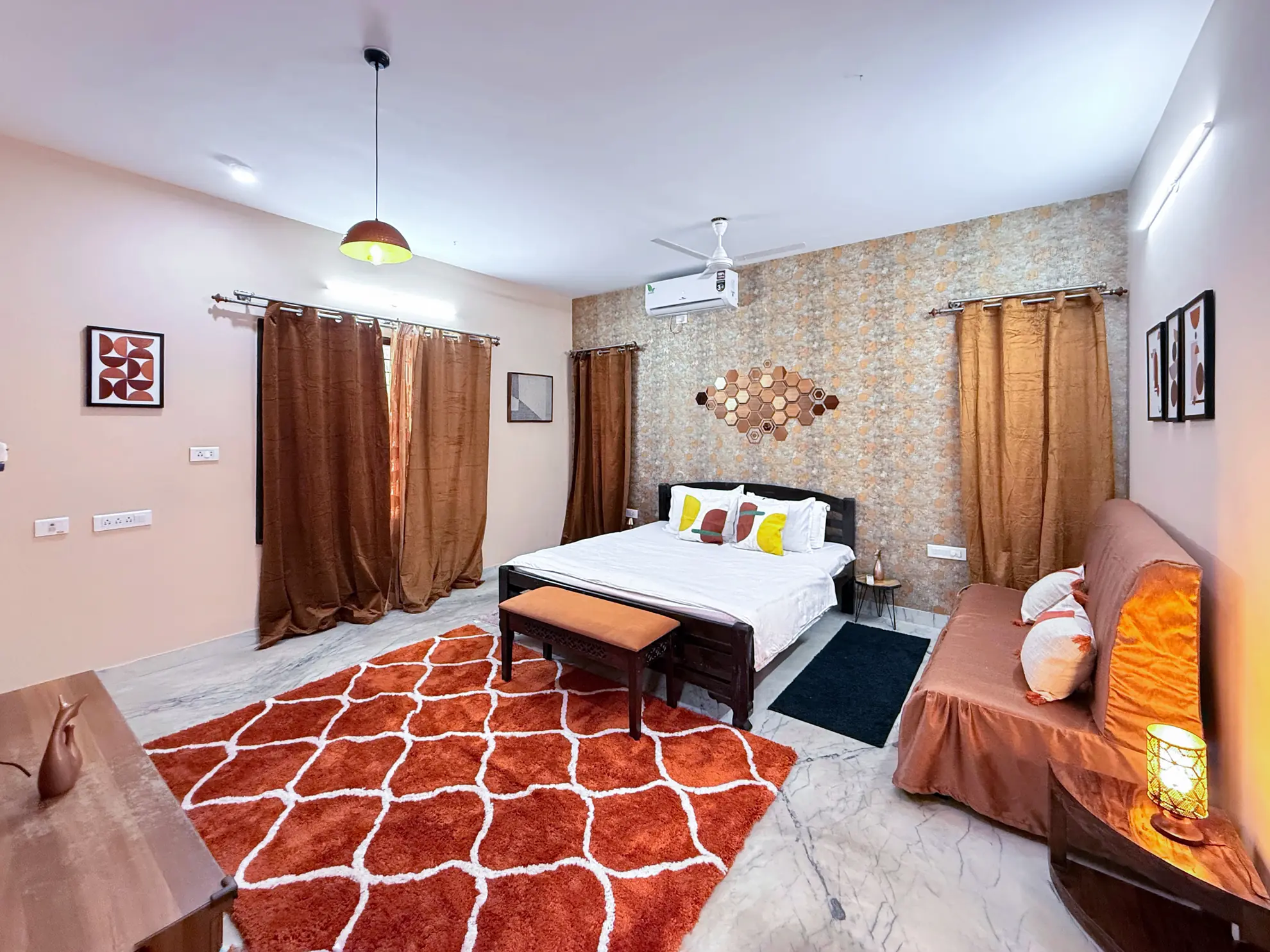 Bedroom with a double bed, orange patterned rug, wall-mounted air conditioner and a sofa with cushions.