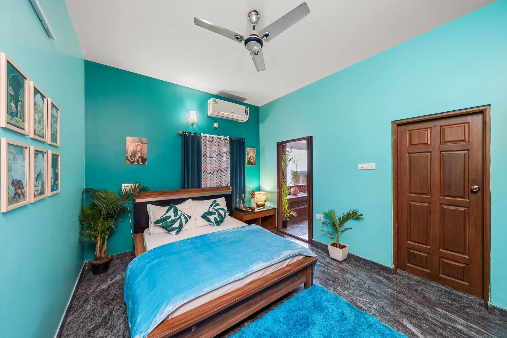 Bedroom with teal walls, a wooden double bed with blue throw, framed prints, and a wall-mounted air conditioner.