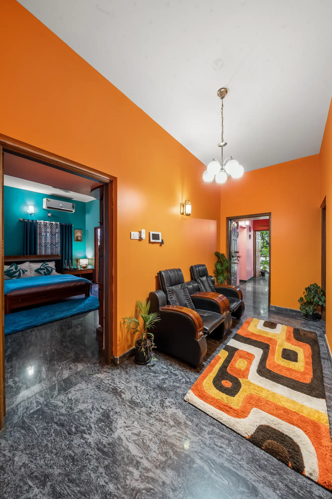Bright orange hallway with two leather recliners, a patterned rug, and a view into a teal bedroom with an air conditioner.