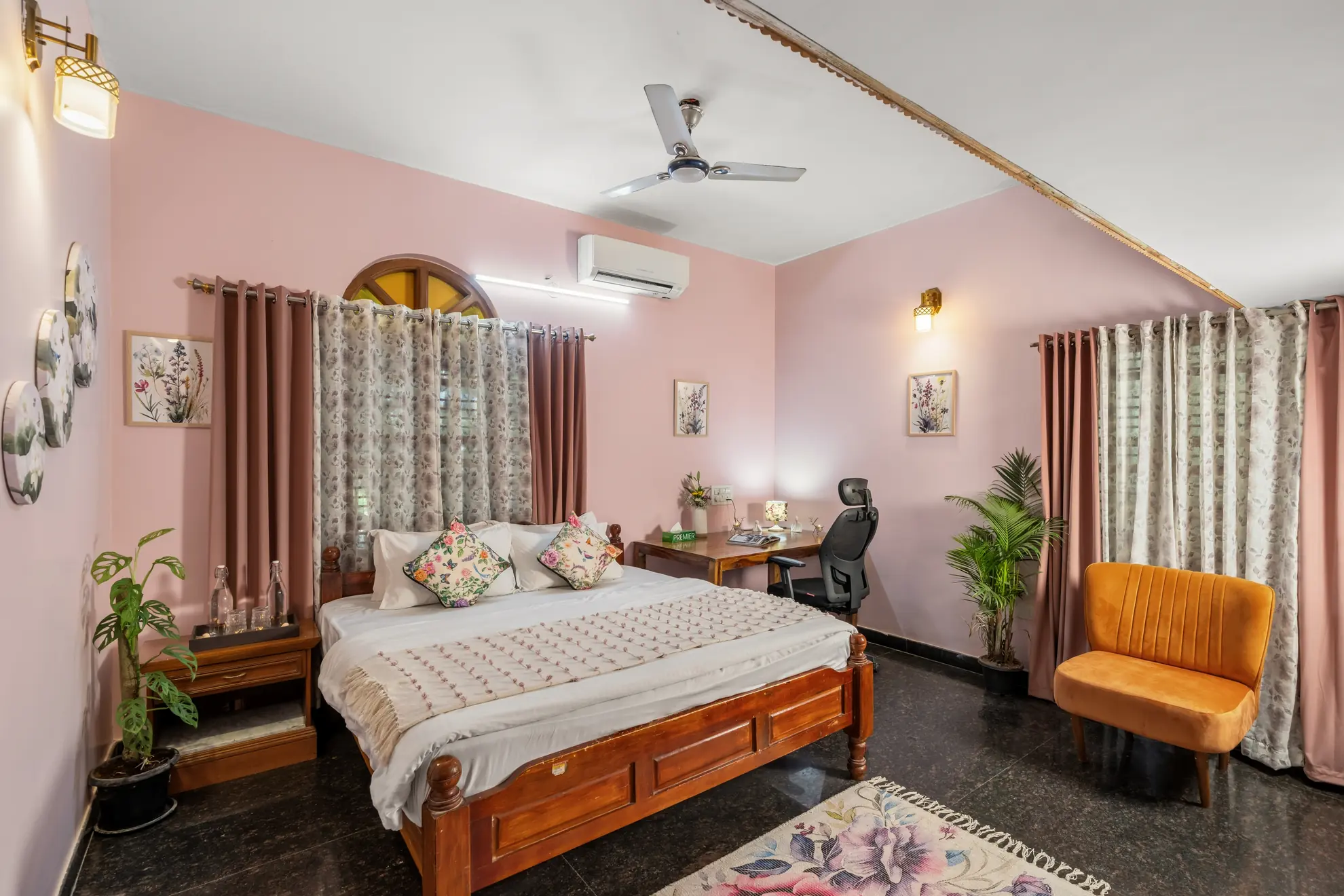 Pink bedroom with a wooden double bed, orange accent chair, desk and wall-mounted air conditioner.