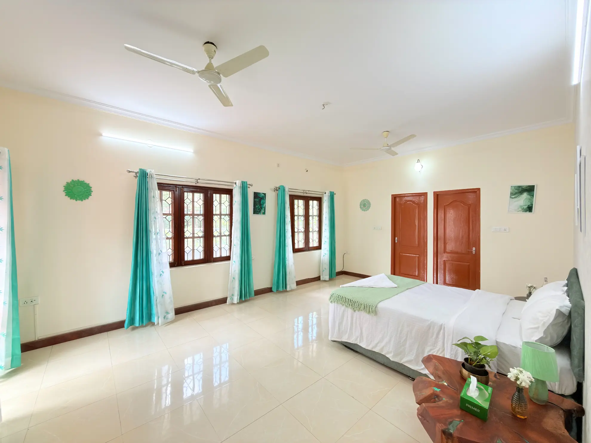 Large bedroom with a double bed, teal curtains, wooden windows and tiled floor, plus two wooden doors.
