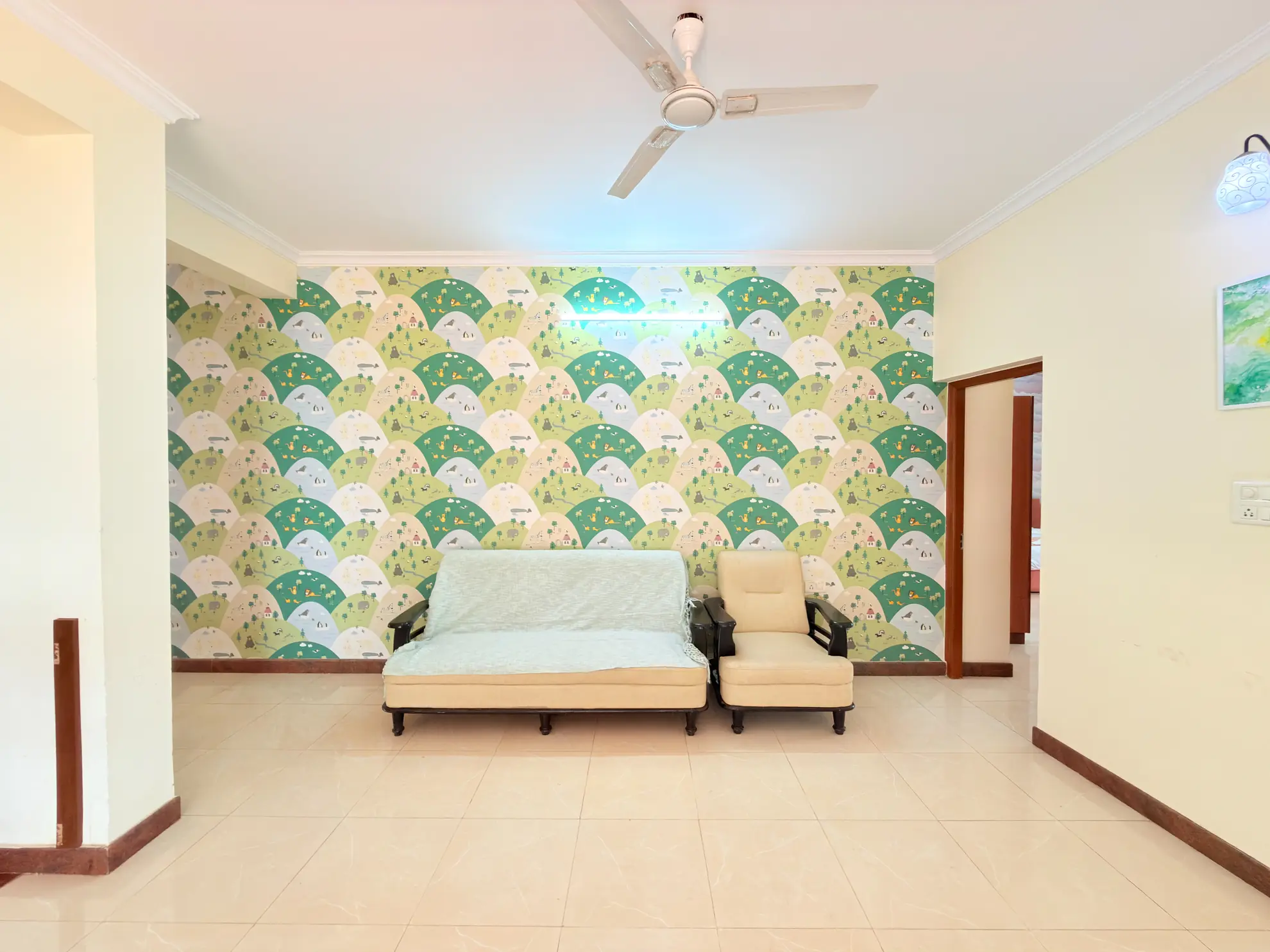 Empty lounge with a patterned green wall, a cream sofa and armchair, and a ceiling fan.