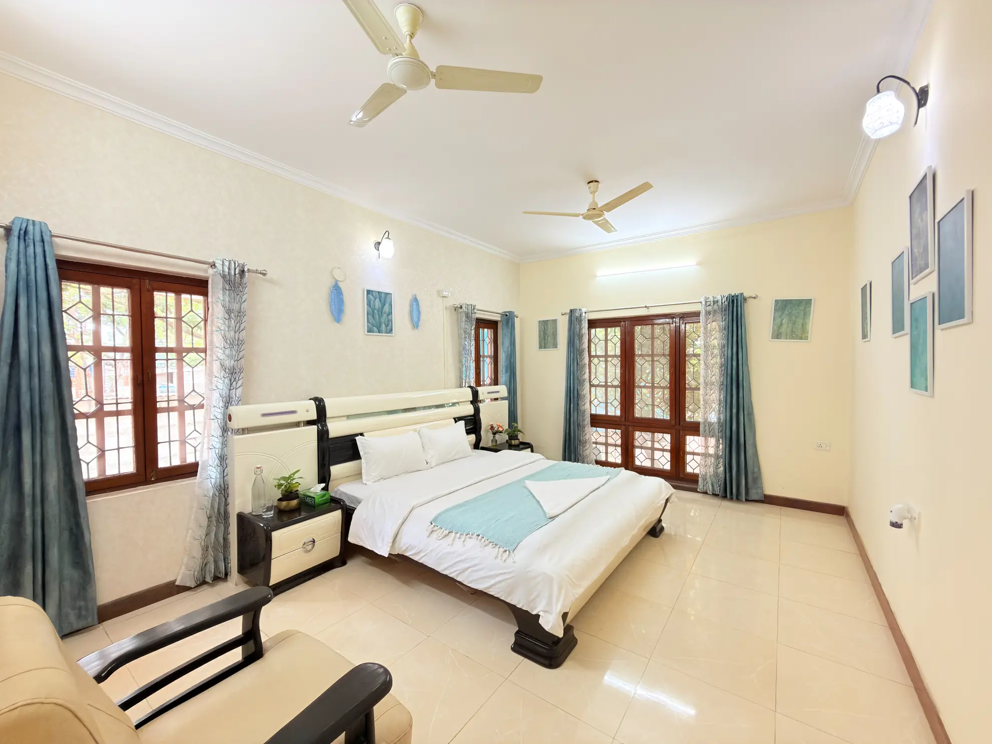 Bedroom with a large white bed, teal throw, ceiling fans, and tall wooden windows with patterned glass.
