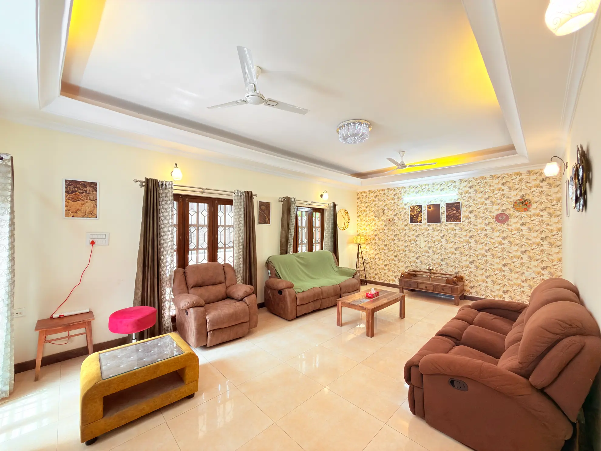 Living room with two brown recliner sofas, a wooden coffee table, ceiling fans and a patterned feature wall.