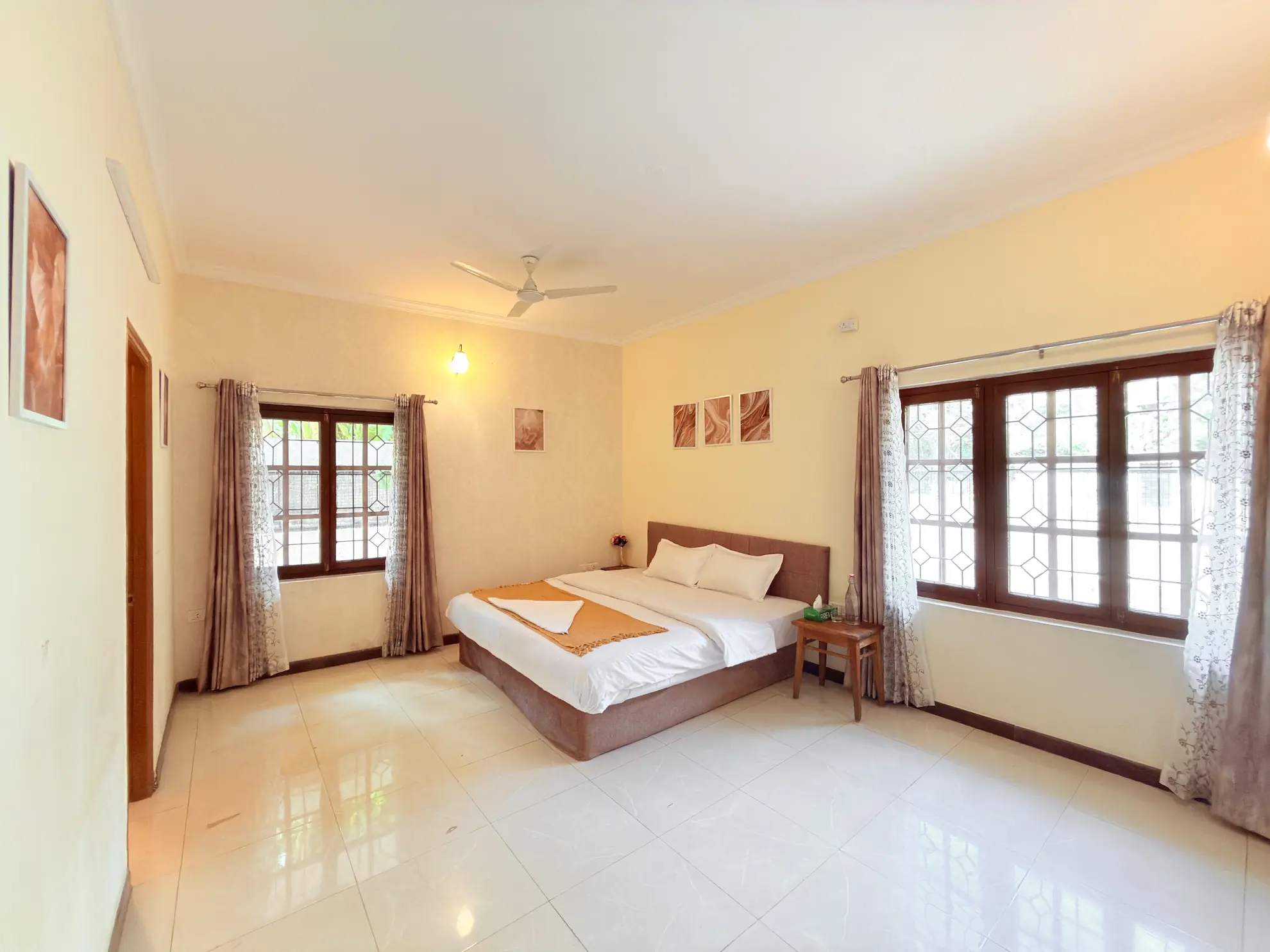 Bright bedroom with a double bed, tiled floor, and two large windows with decorative grilles.