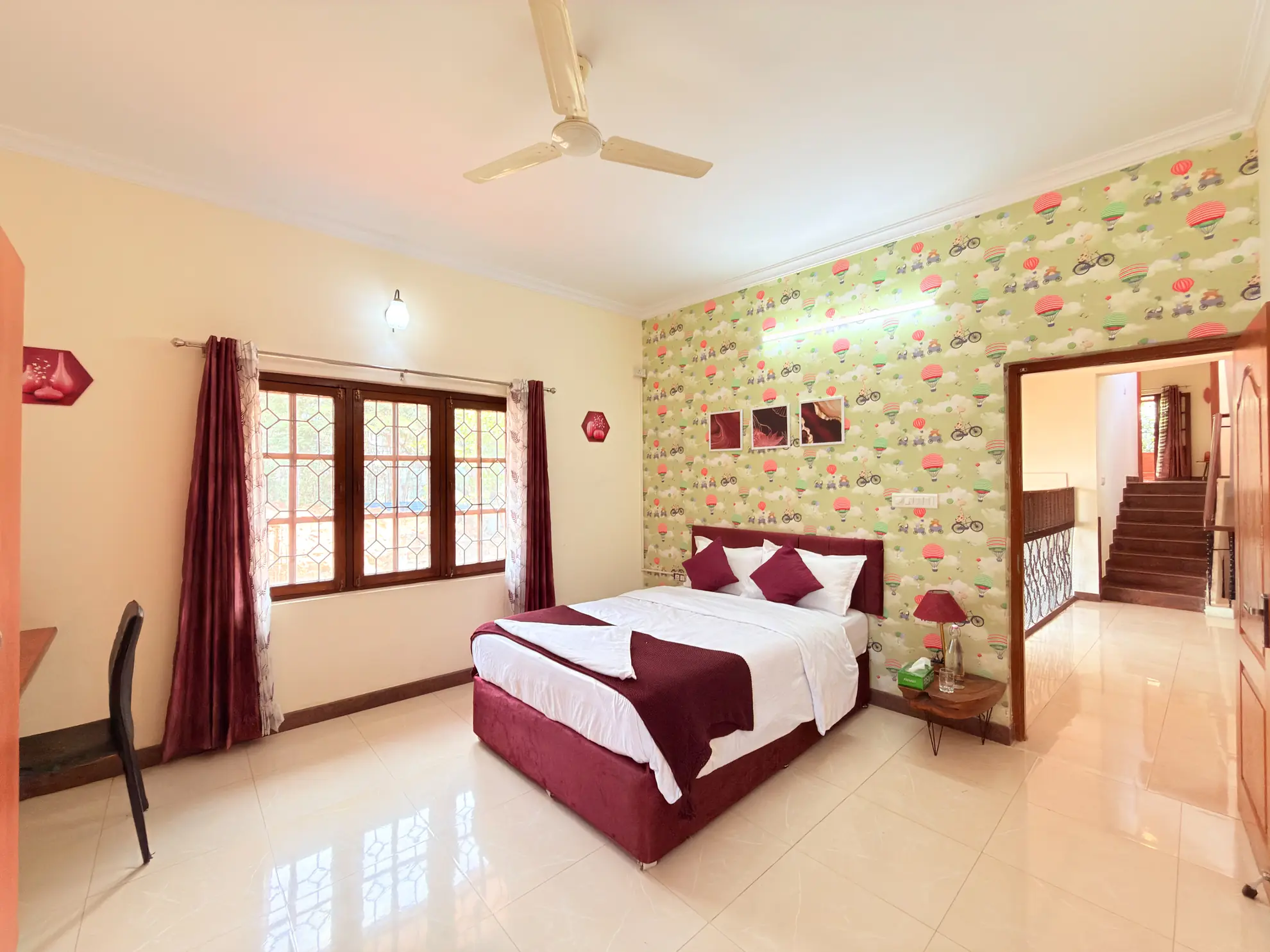 Bedroom with a double bed, patterned hot-air-balloon wallpaper, and leaded wooden windows with a ceiling fan.
