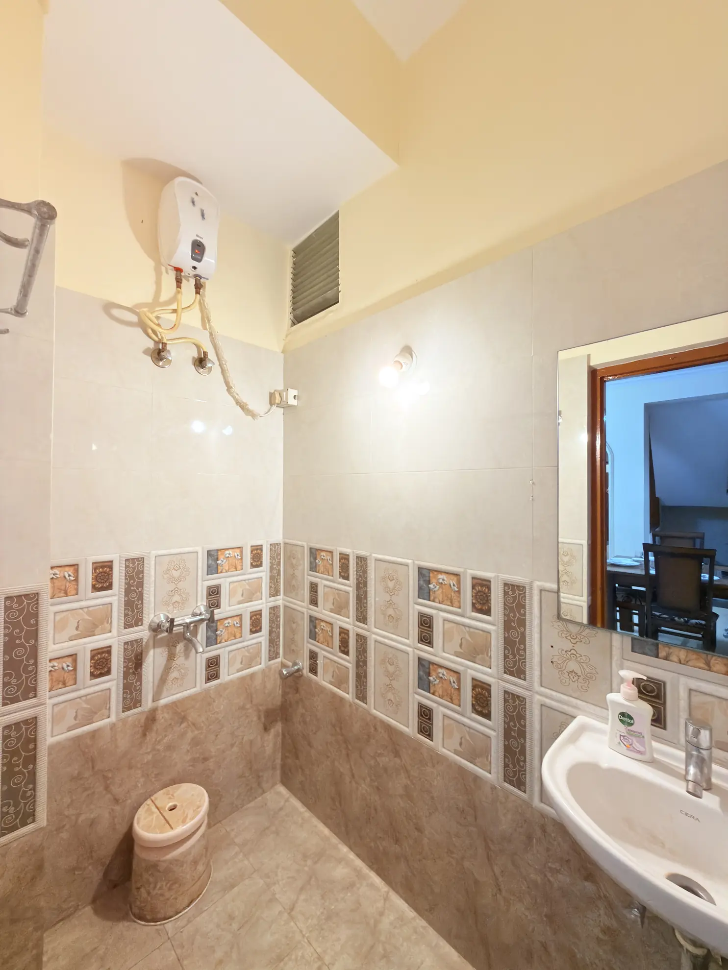 Bathroom with a wall-mounted electric water heater, patterned tile walls, and a pedestal sink with soap dispenser.