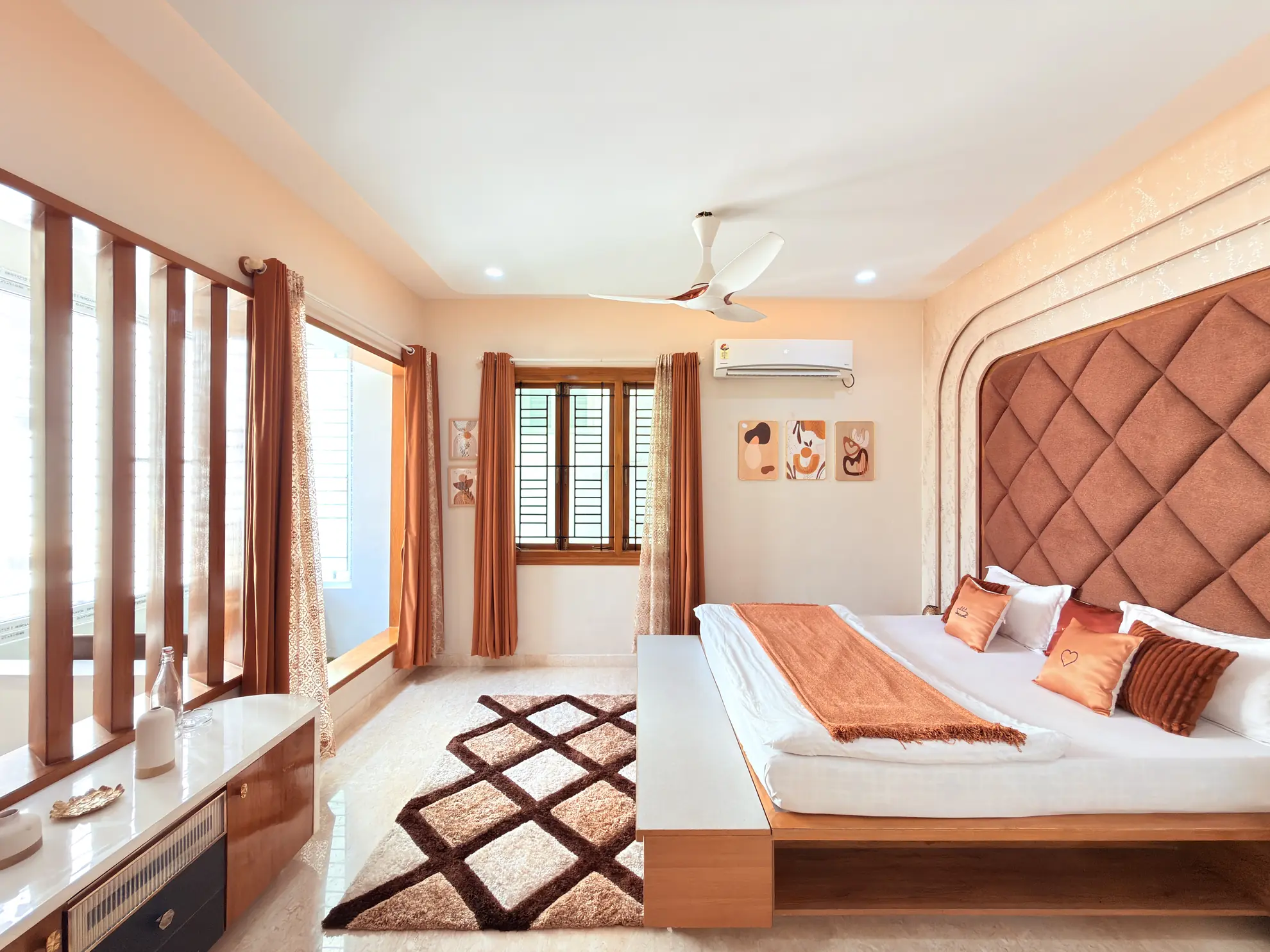 Bedroom with a large quilted headboard, orange curtains, ceiling fan and wall-mounted air conditioner.