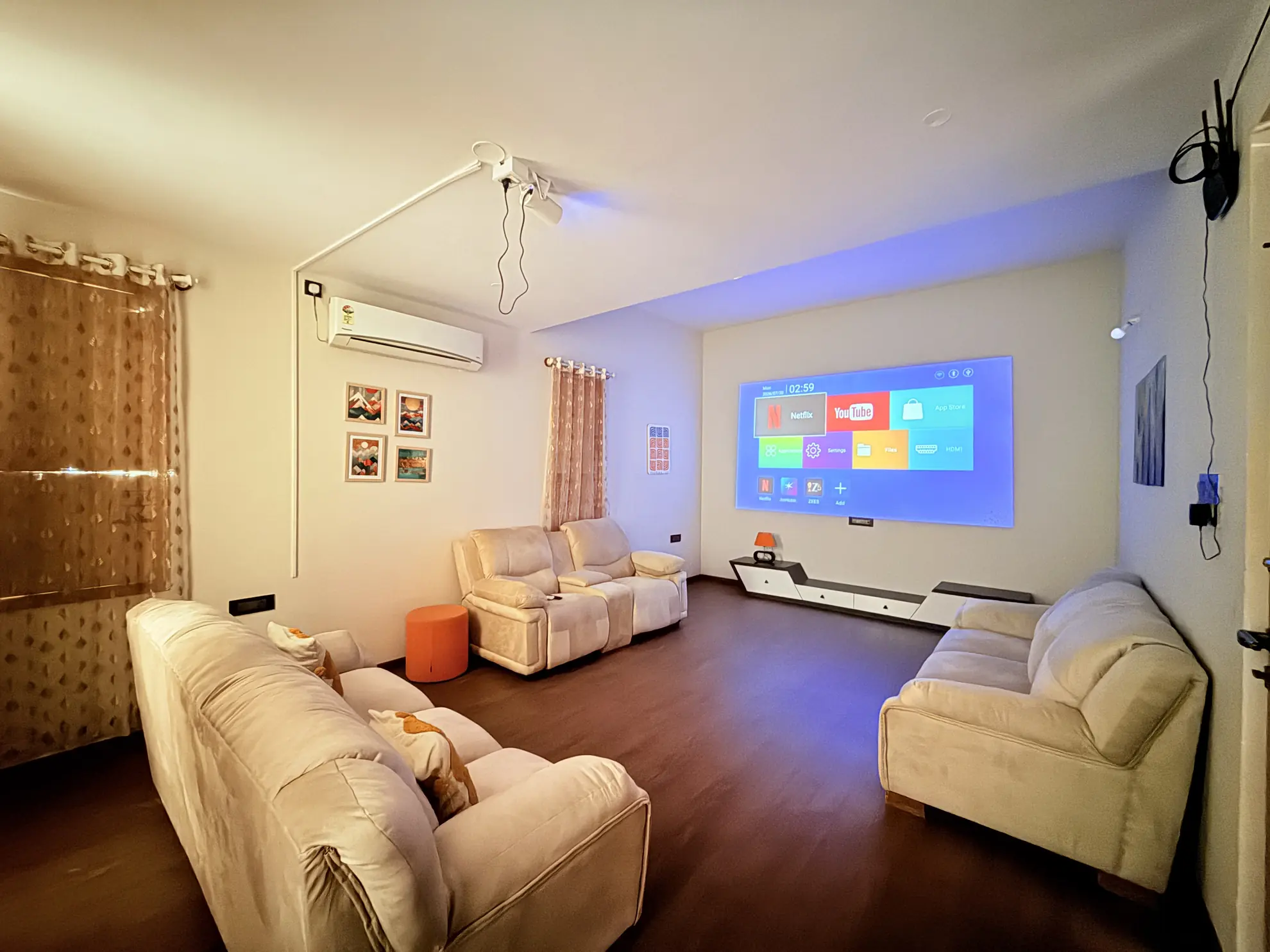 Home theatre room with a wall-mounted projector screen, two cream sofas and a reclining loveseat.