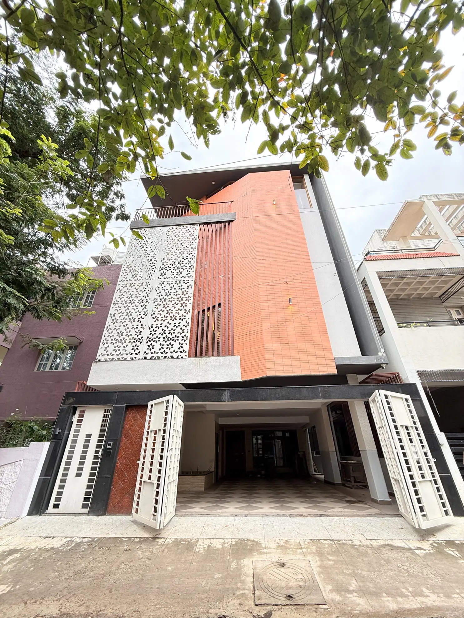 Front elevation of a multi-storey villa with a perforated white screen, terracotta facade, and an open ground-floor parking bay.