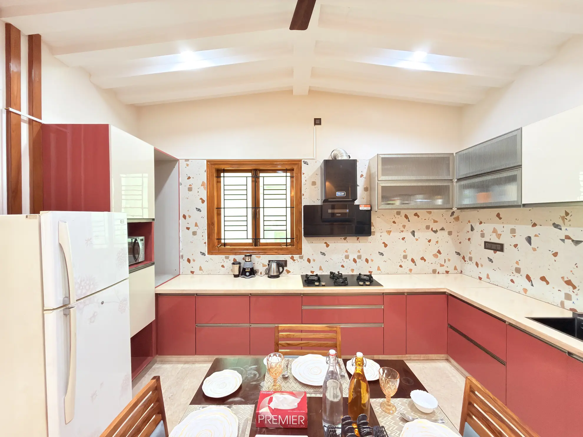 Kitchen with red cabinets, terrazzo backsplash, gas hob and a dining table set for two in the foreground.