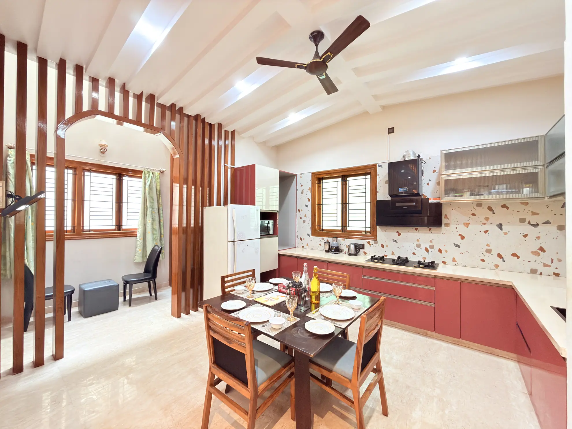 Open-plan dining area with a wooden dining table set for four, next to a red-fronted kitchen with a gas hob and fridge.